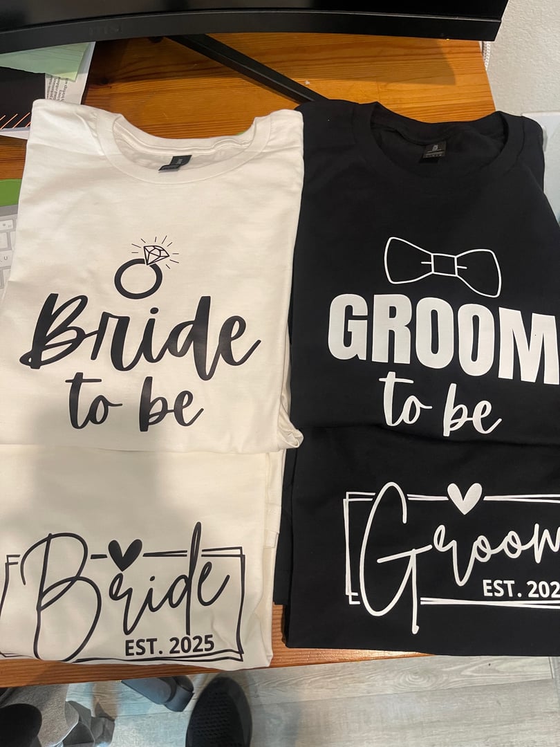 White and black shirts with Bride to be and Groom to be designs, featuring wedding rings and bow tie graphics, Est. 2025.