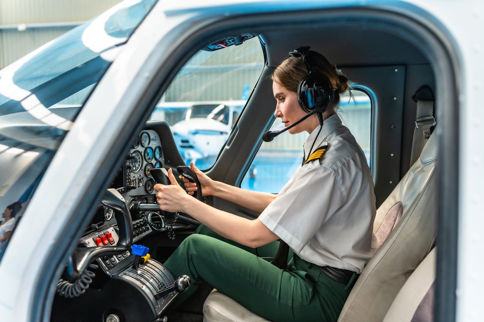 Confident female pilot sitting in the cockpit of a small airplane, preparing for takeoff, holding the controls and wearing a headset