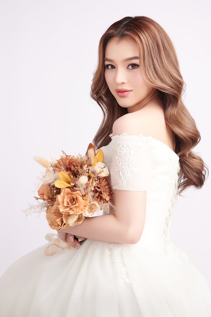 Beautiful young asian woman in wedding dress holding bouquet on white background,