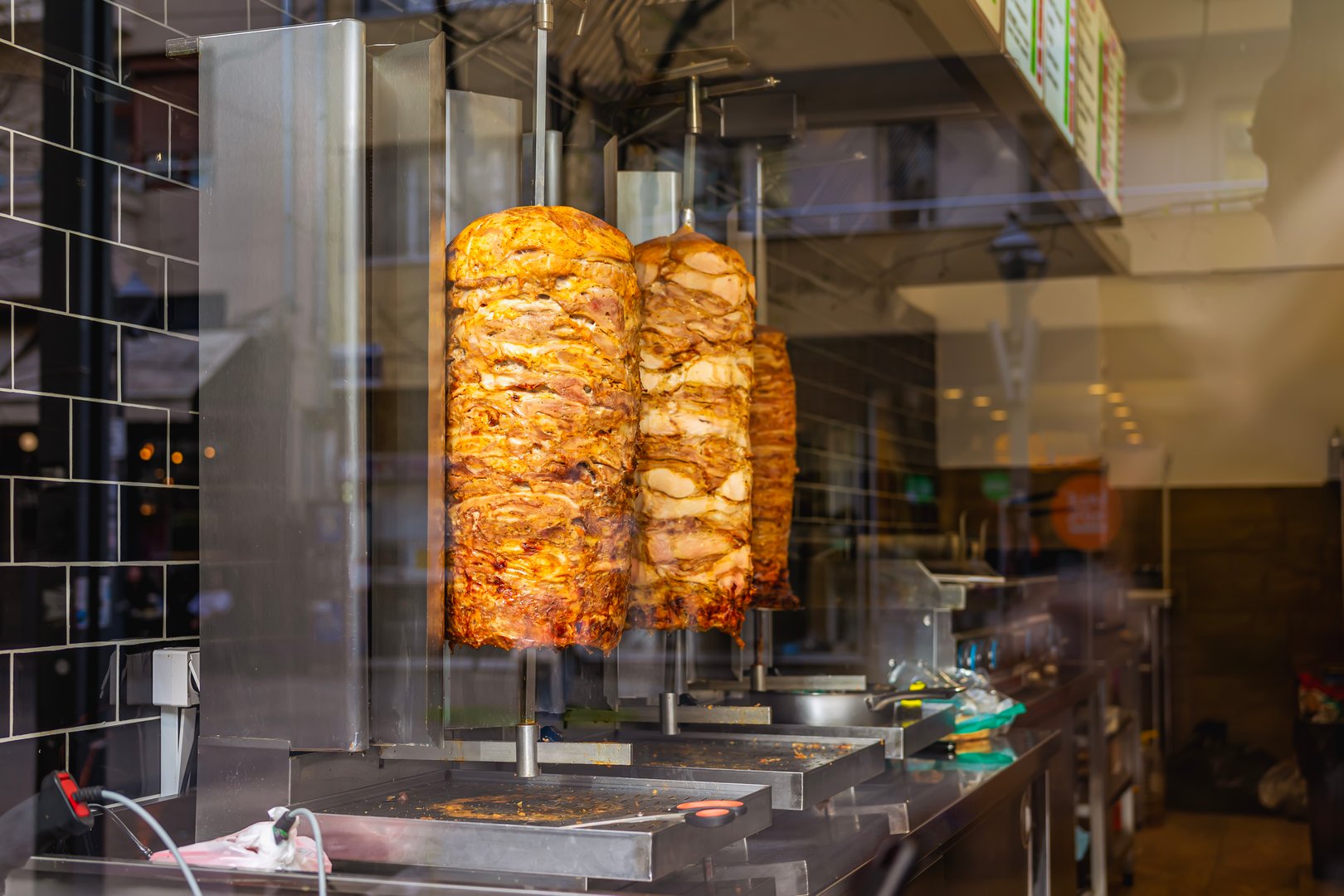 Traditional street food doner kebab or shawarma on vertical rotisserie. Rotating shawarma meat grilling on spit inside street food shop. Concept of street food, fast food culture, authentic cuisine