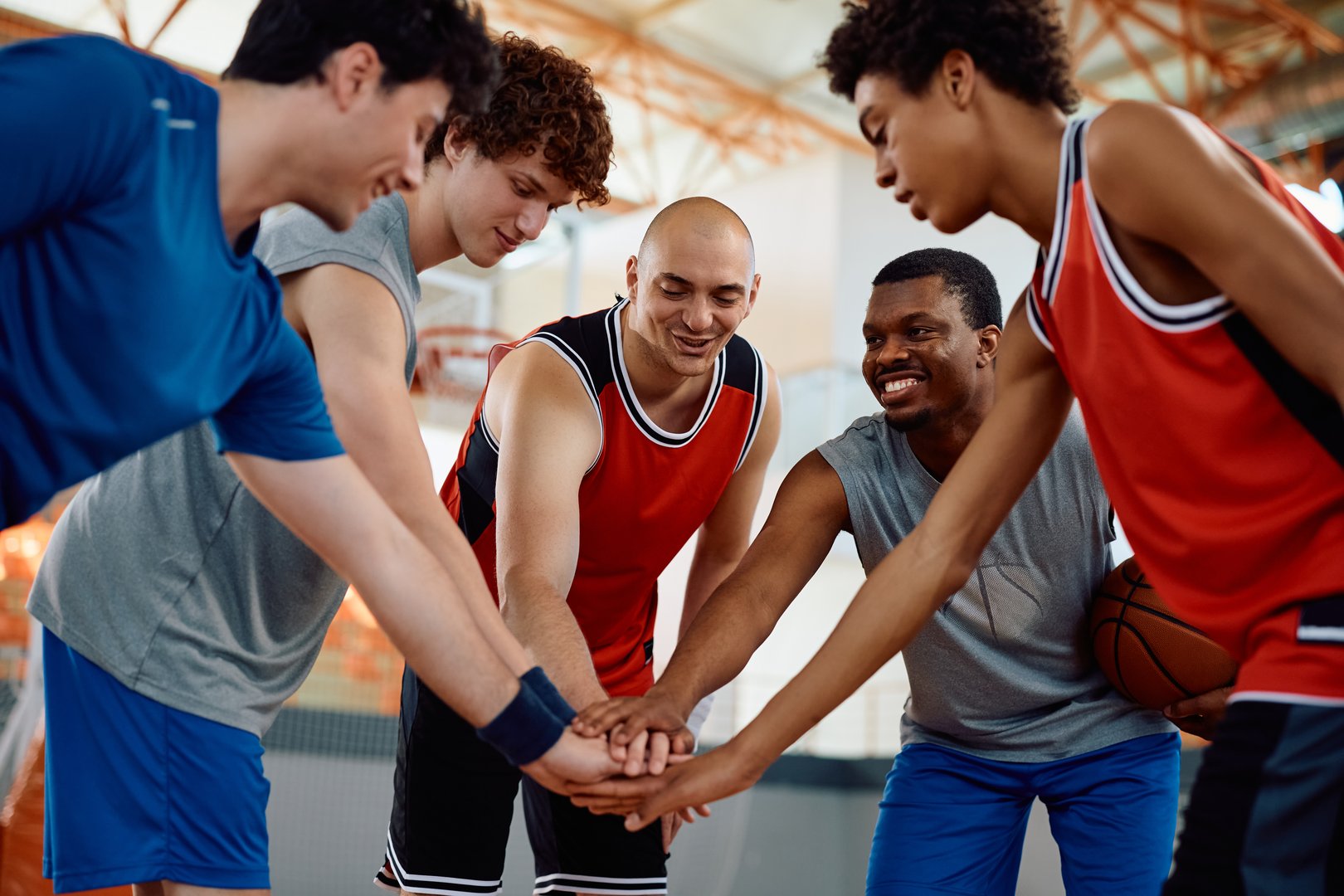 Happy basketball team gathering hands in unity before the match at school gymnasium.