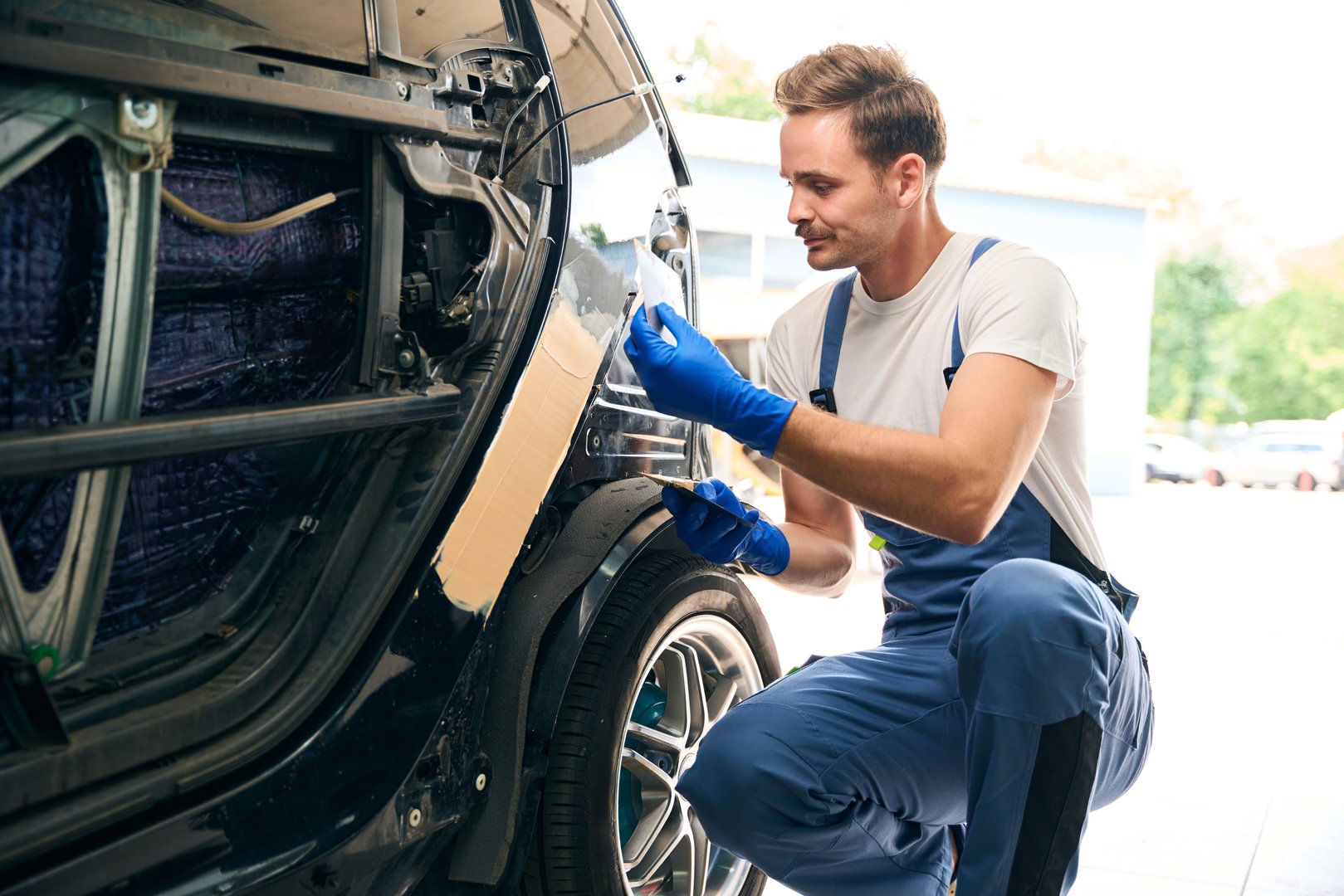 Male worker preparing car for painting in a workshop, applying putty to the car before painting. Repair after an accident
