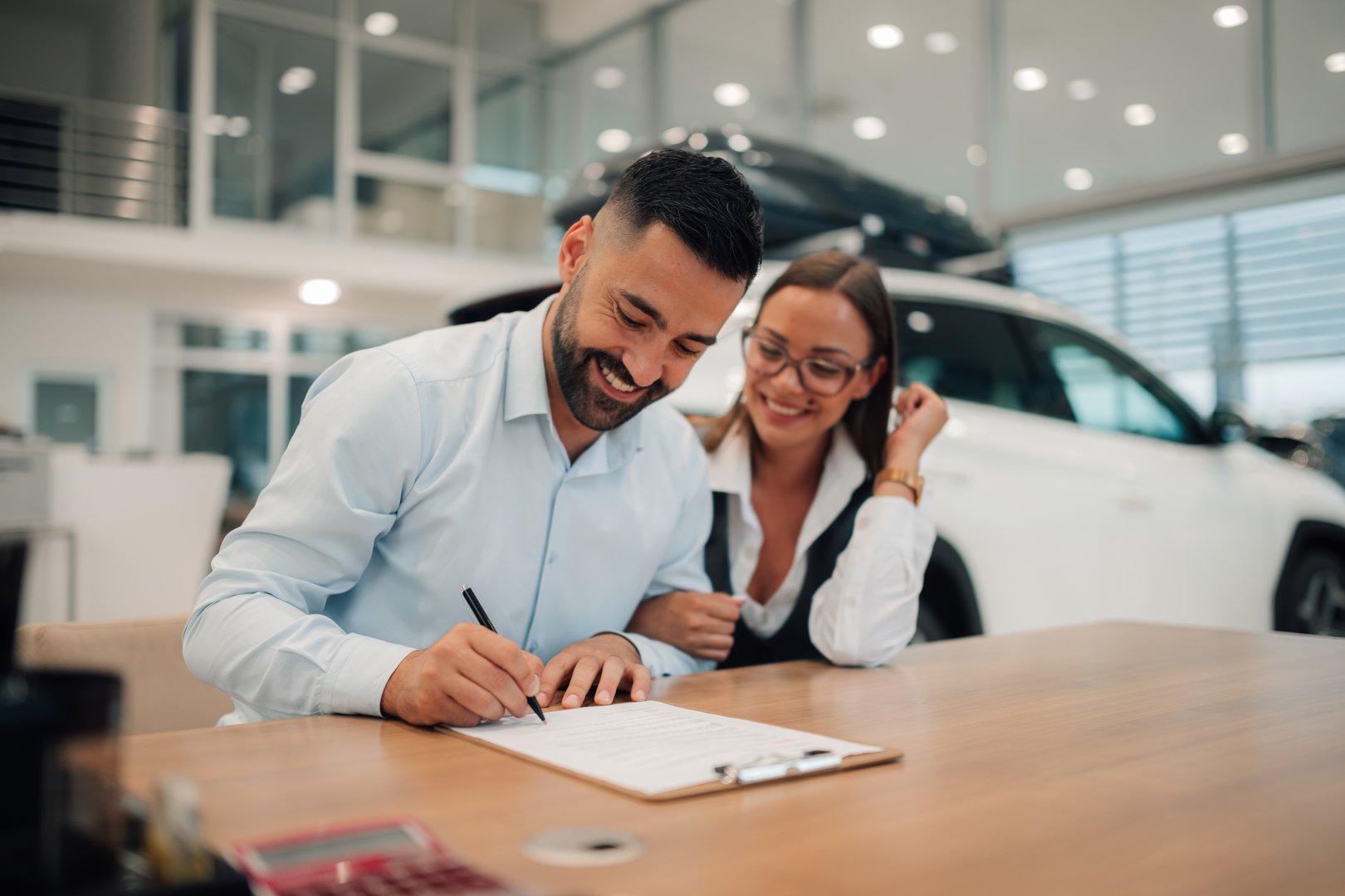 A couple joyfully completes the signing process for their new car purchase at a dealership, sealing their commitment and excitement for their forthcoming journeys together.