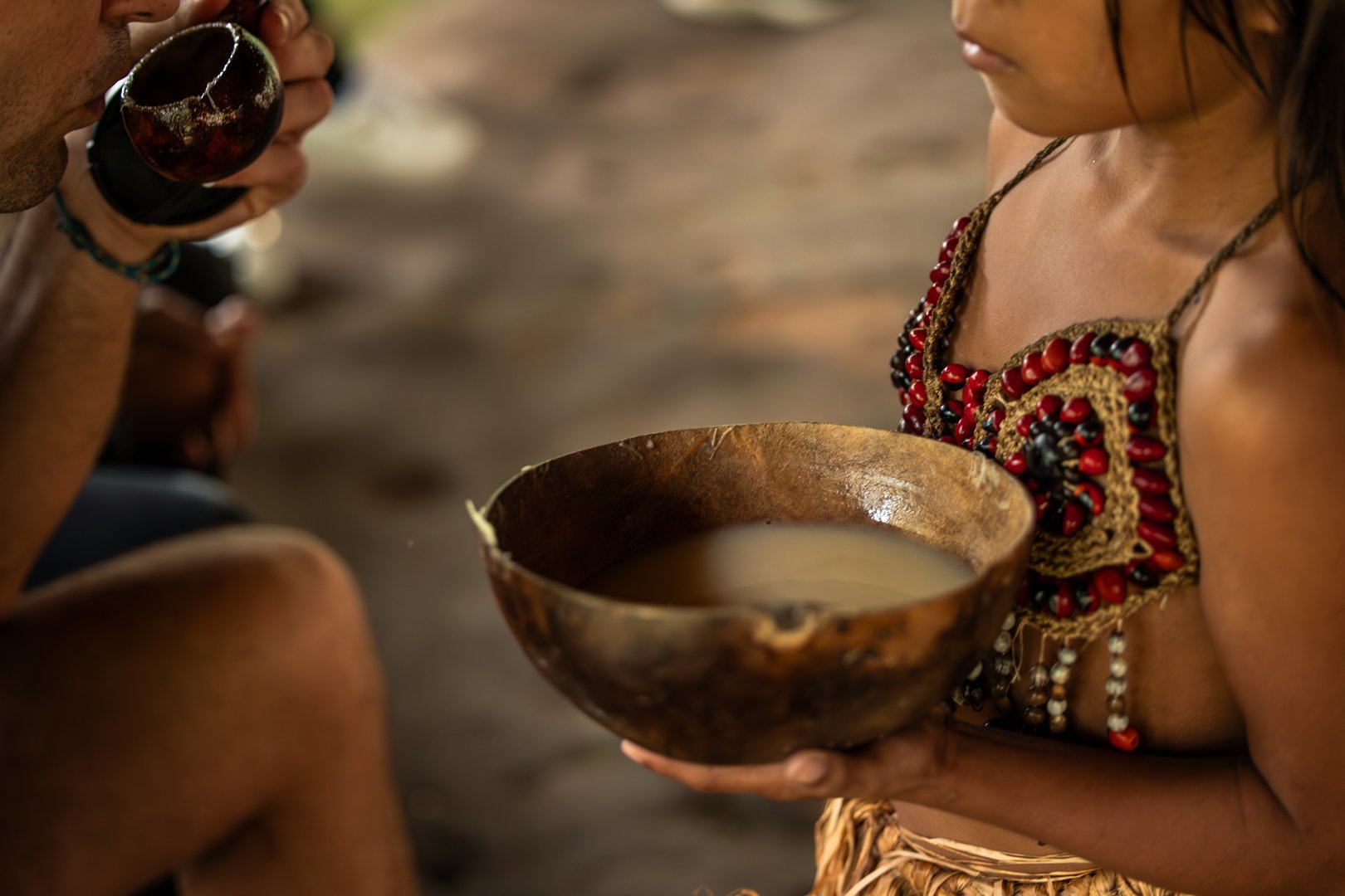 Closeup of a Wayuri indigenous girl presenting a bowl of Chicha drink to a tourist in the Ecuadorian Amazon. This image captures a cultural exchange moment