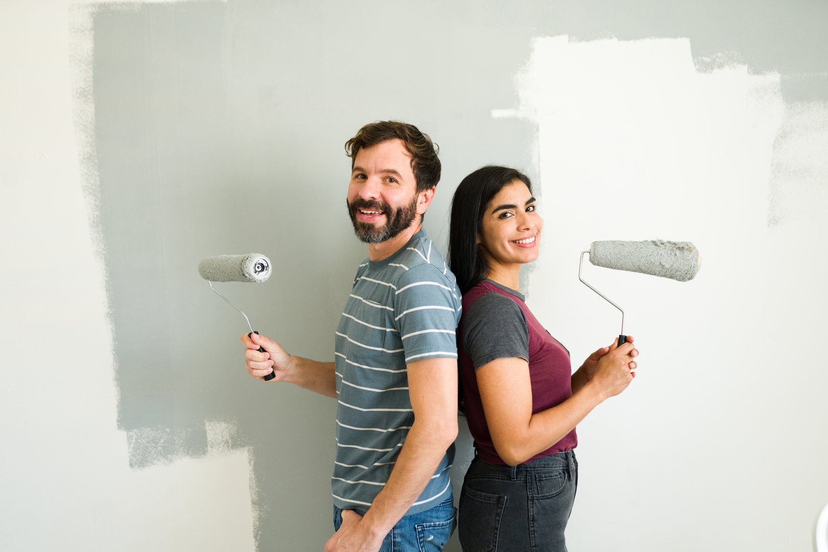Happy couple is having fun while painting the walls of their new apartment using paint rollers