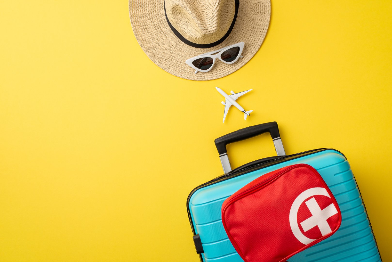 Flat lay image displaying summer travel essentials including a suitcase, hat, and sunglasses on a bright yellow background, evoking wanderlust and preparedness