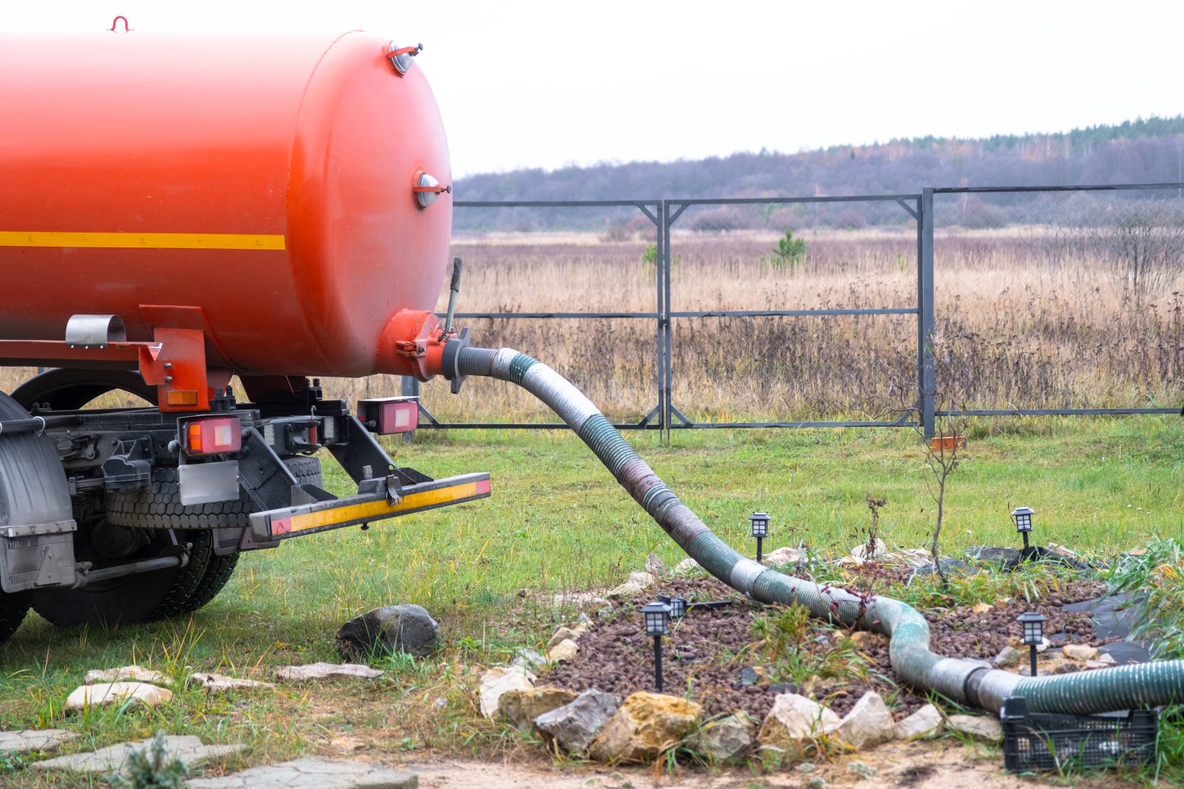 The orange tank of the sewage disposal machine in the courtyard of the house sucks sewage waste from the septic tank well. Waste disposal service, sewage disposal