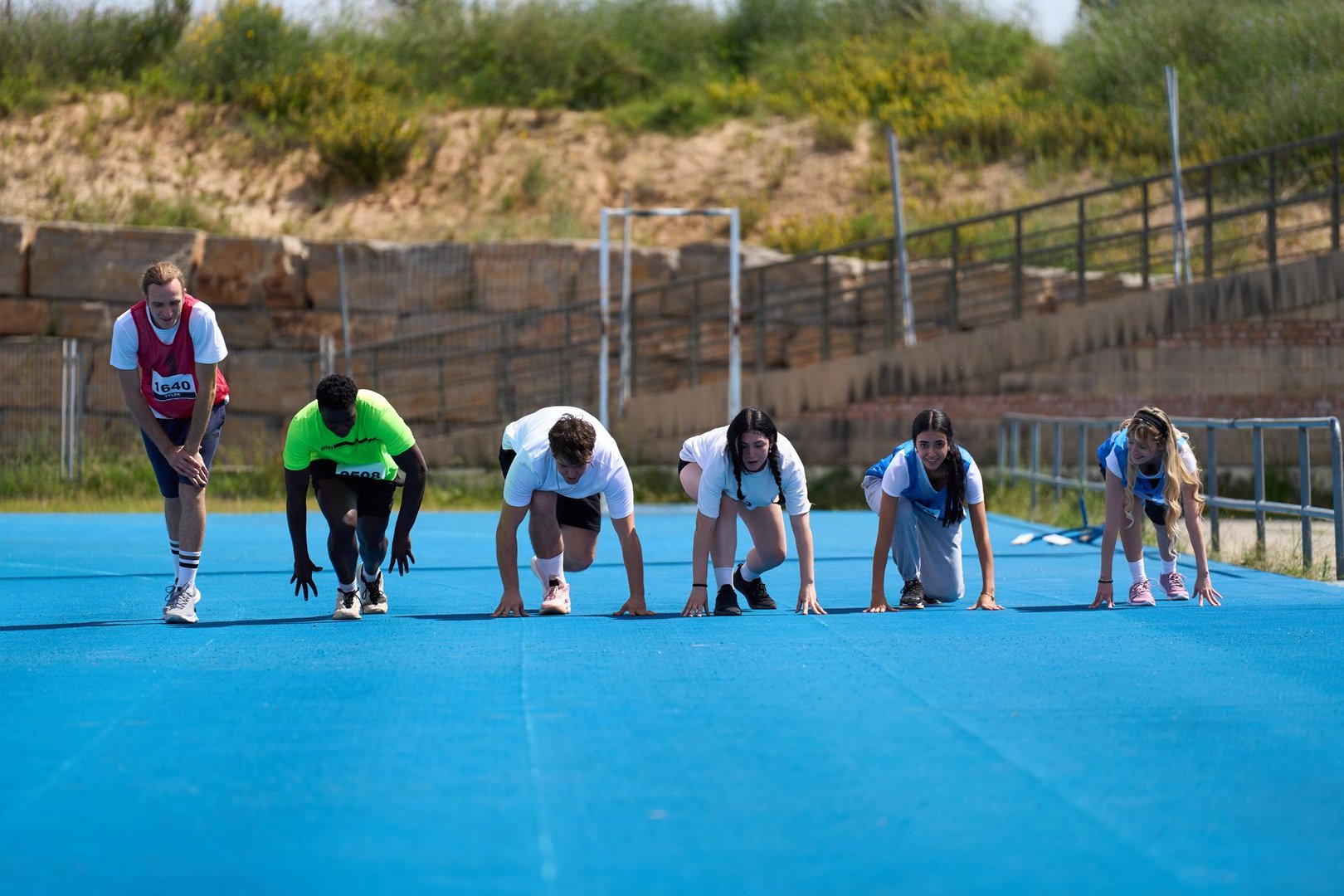 Diverse group of athletes poised at the starting line, focused and determined, ready to race on a vibrant blue running track