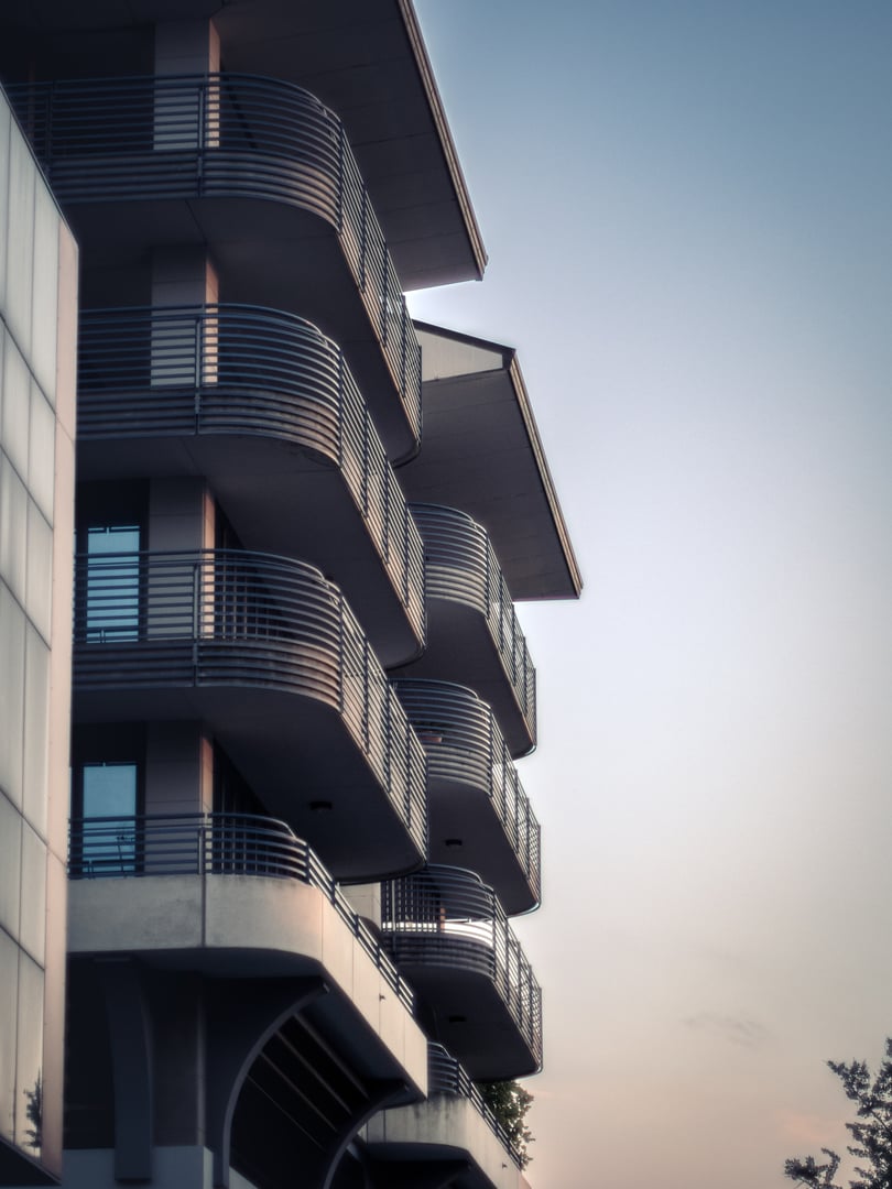 Contemporary hotel facade featuring sleek balconies and large glass windows, reflecting the sky in soft evening light. Clean lines and modern architectural style.
