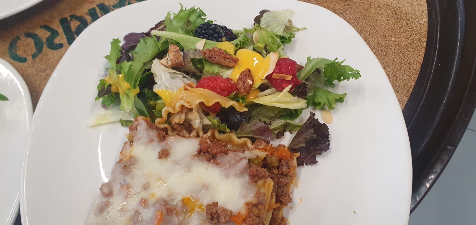 Plate with a serving of lasagna beside a mixed green salad topped with berries and nuts.