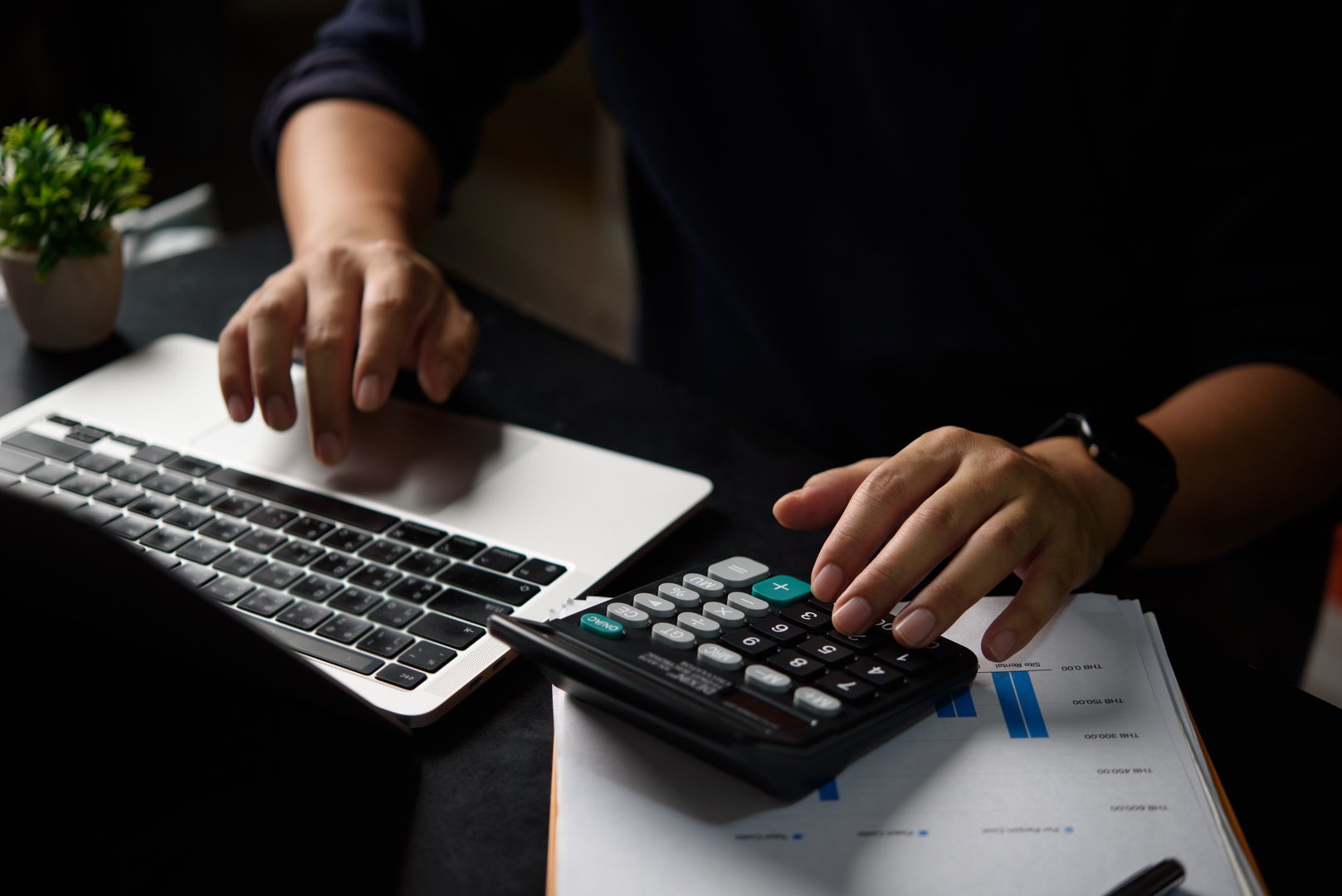 Professional accountant calculating tax expenses using calculator reviewing financial statement. Business finance expert performing budget analysis with modern accounting software and digital tools.