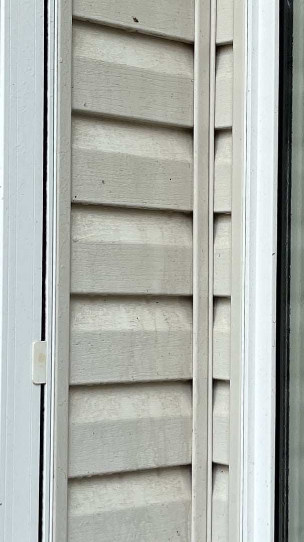 Close-up of beige siding next to white door frame with visible rain streaks and small specks of dirt.