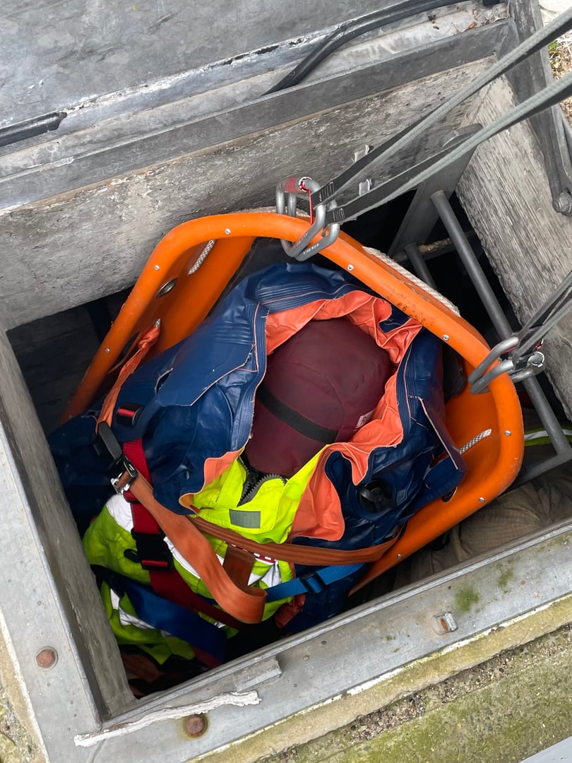 Rescue operation with a person in safety gear being lifted from a manhole using a stretcher and harness.