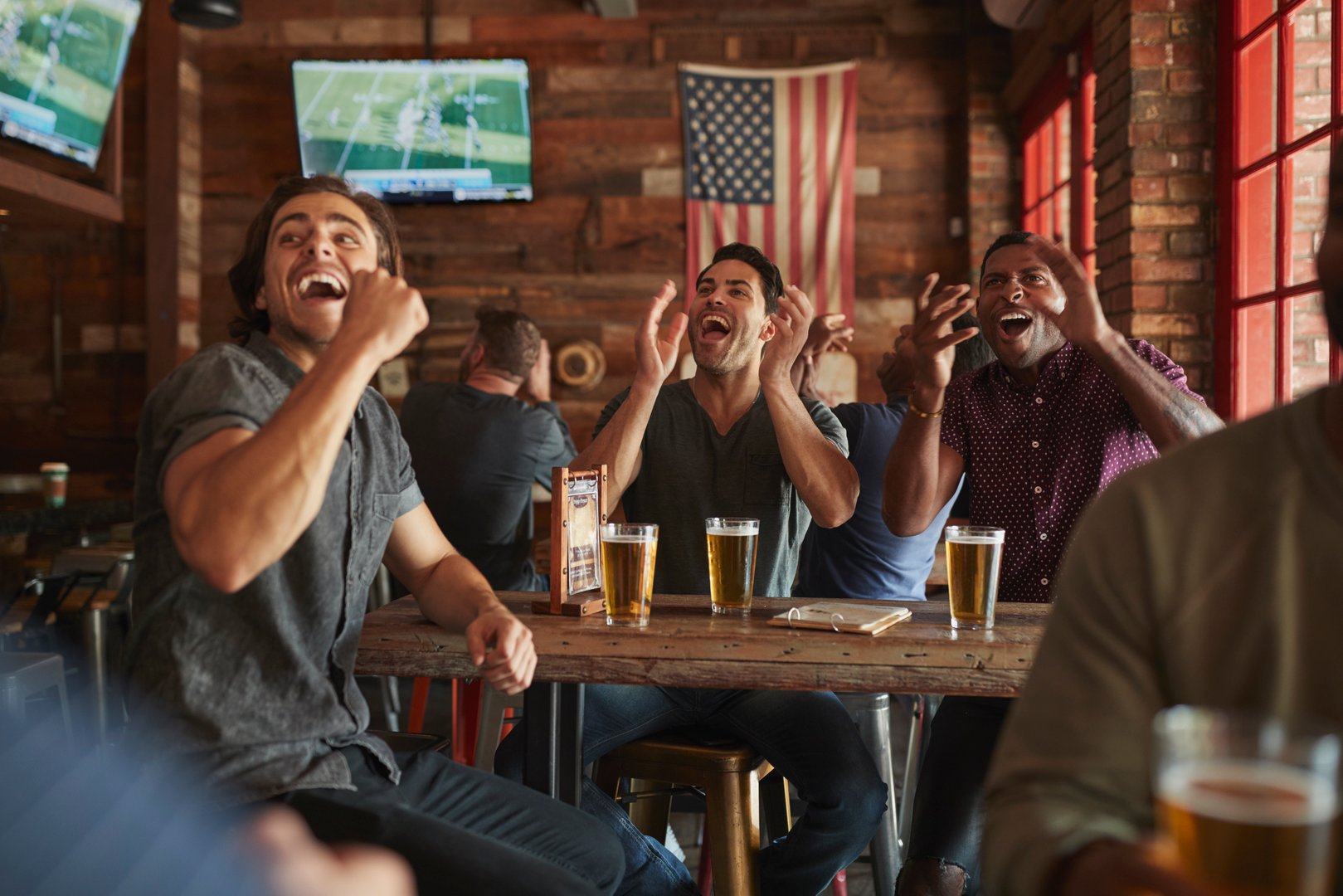Group Of Male Friends Celebrating Whilst Watching Game On Screen In Sports Bar