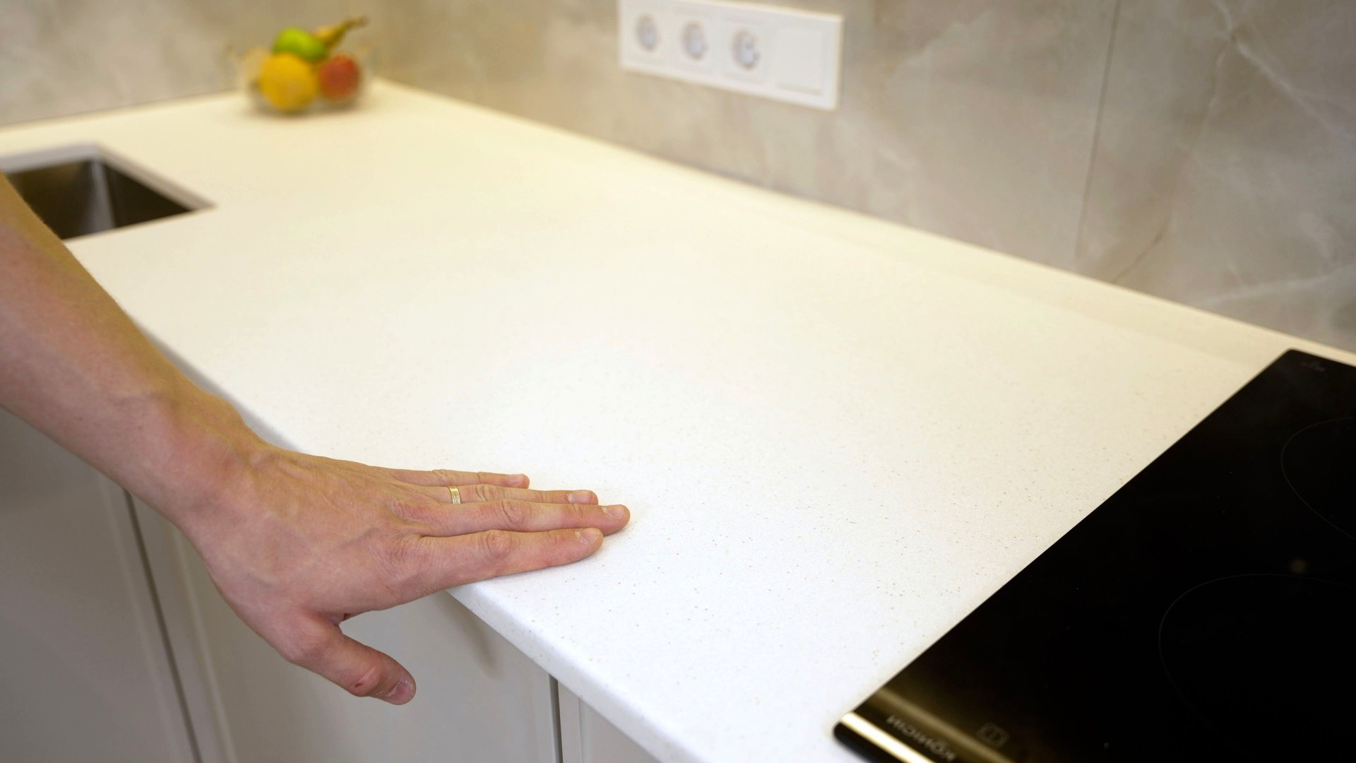 Person is touching a white countertop in a modern kitchen, checking its quality.