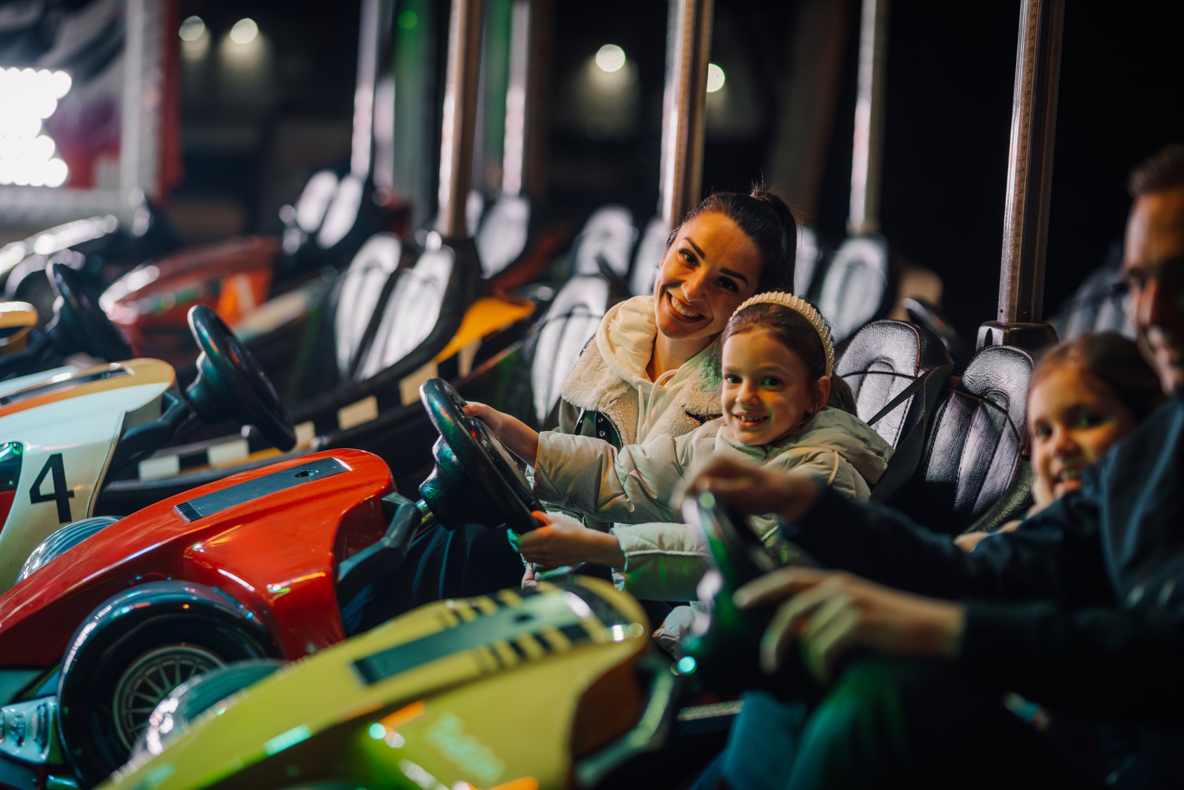 Mother and daughters enjoying driving bumper cars at amusement park, having fun together on weekend evening