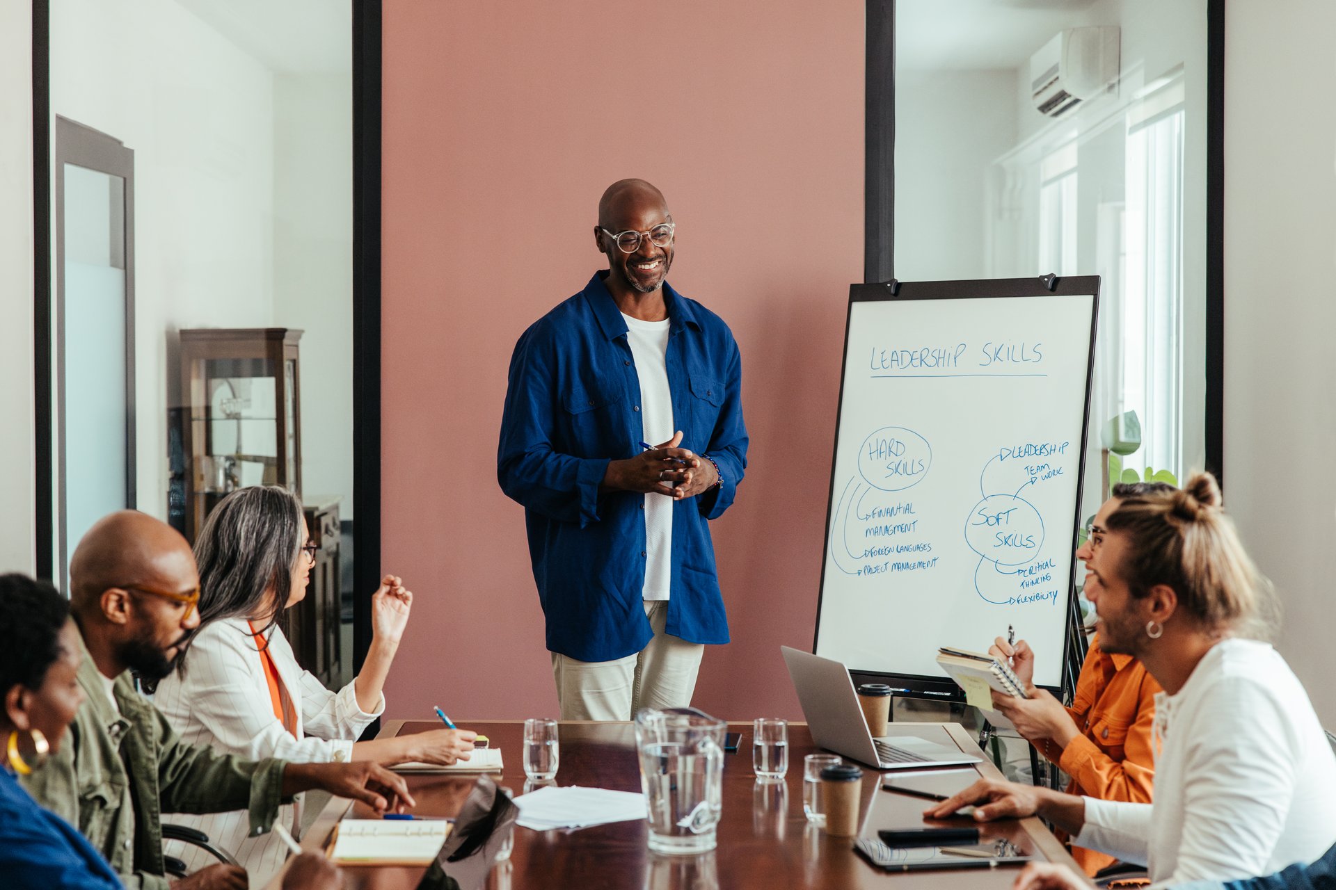 Man leading a relaxed leadership training workshop in a modern office boardroom with a diverse team. Focus on teamwork, hard and soft skills.