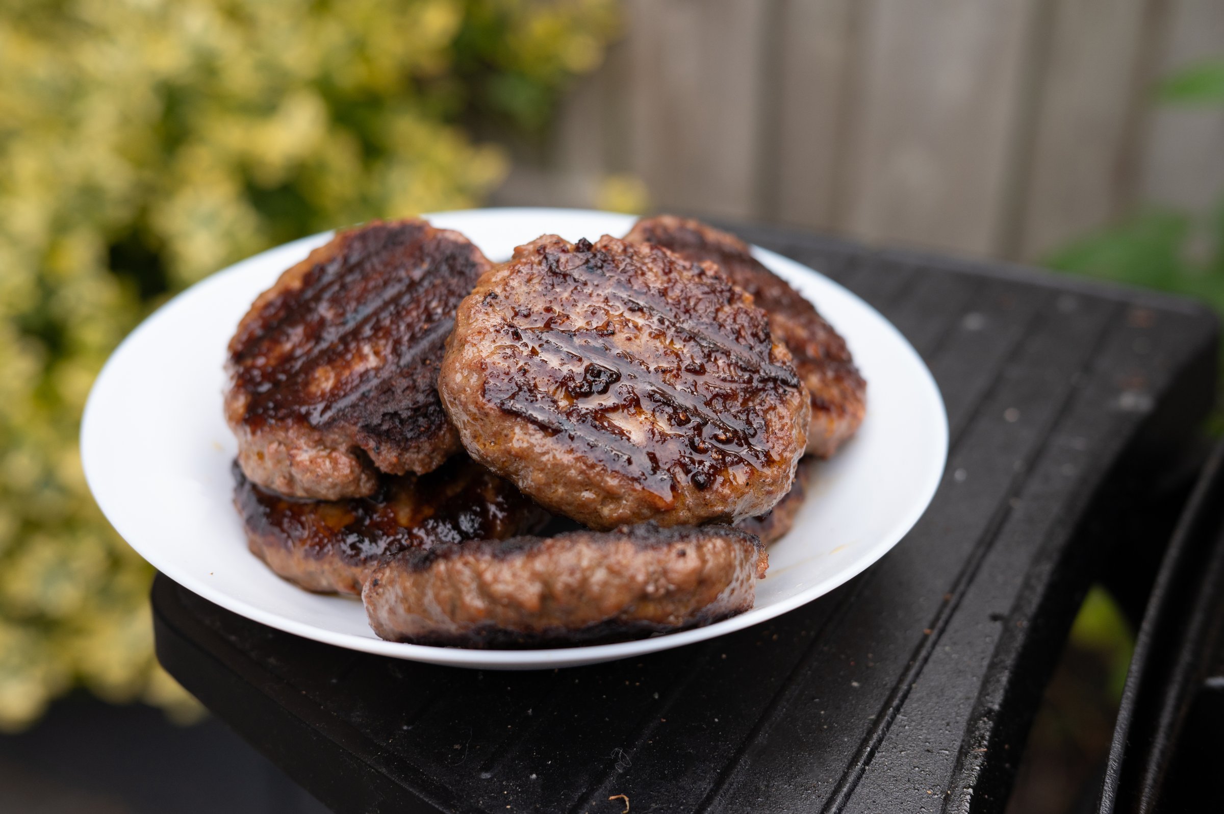 Juicy grilled beef patties on a white plate outdoors.