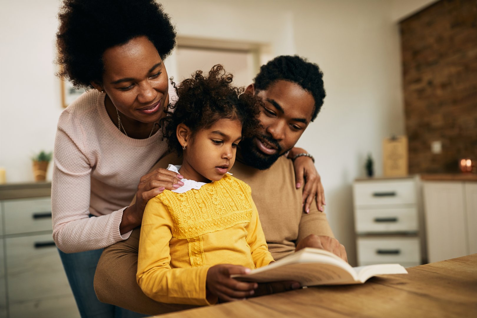 African American parents with daughter reading a book at home.
