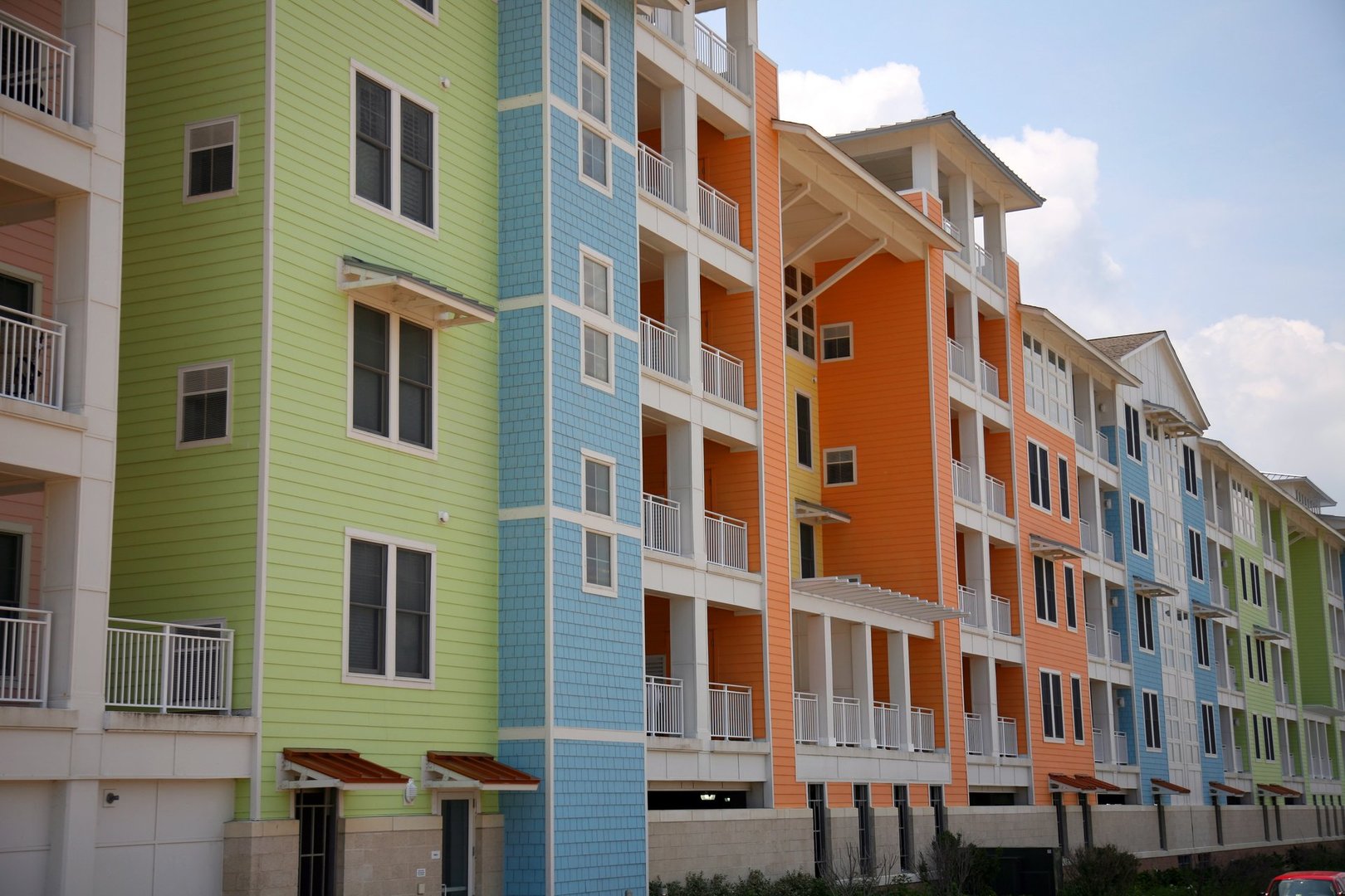 Colorful modern apartment buildings with green, blue, orange, and peach facades under a partly cloudy sky.