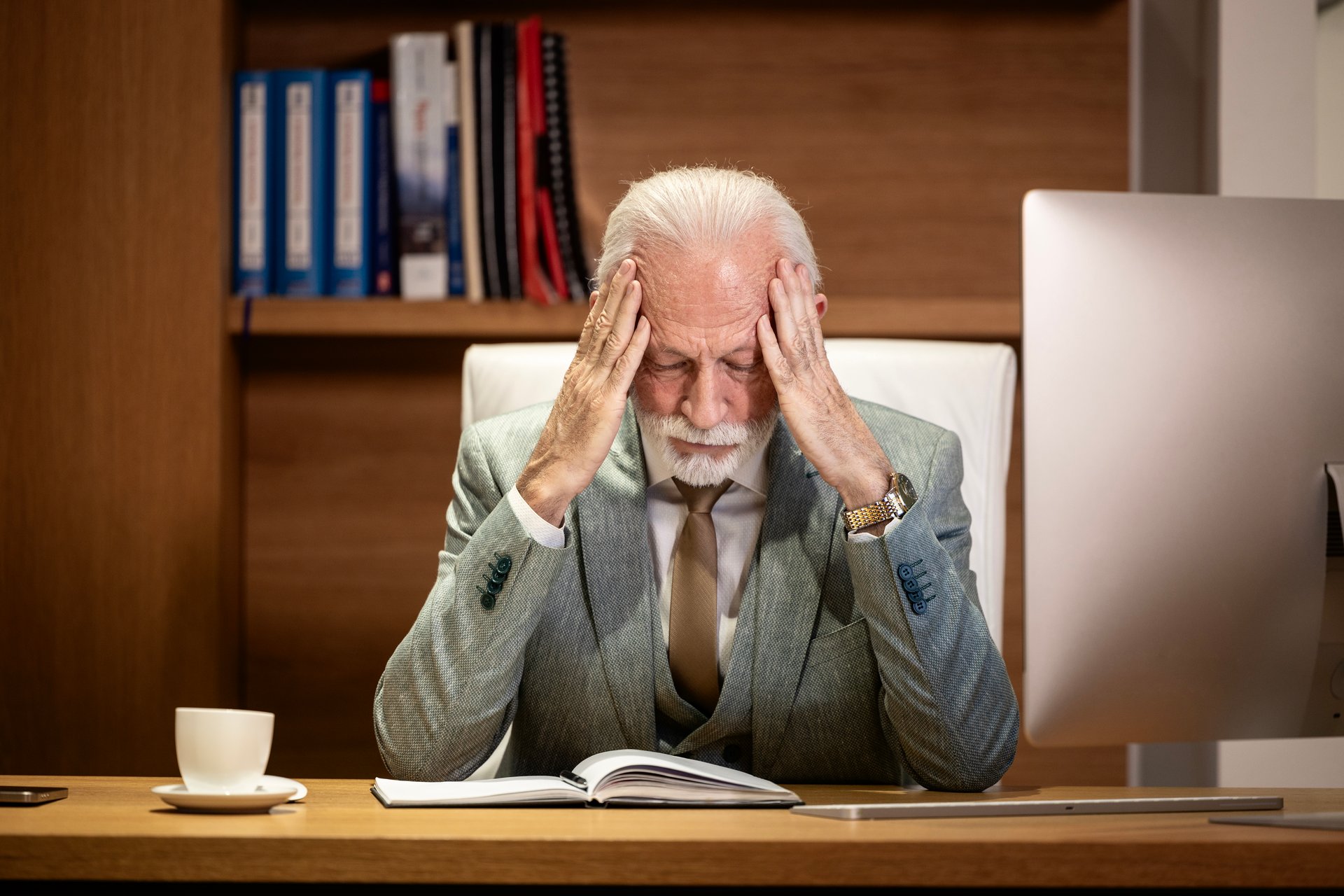 Senior businessman sitting in his office having a headache due to numerous problems in company.