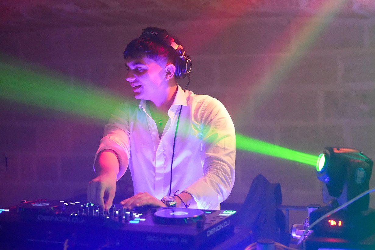 DJ wearing headphones energetically mixing music at a club, with colorful lights illuminating the scene.