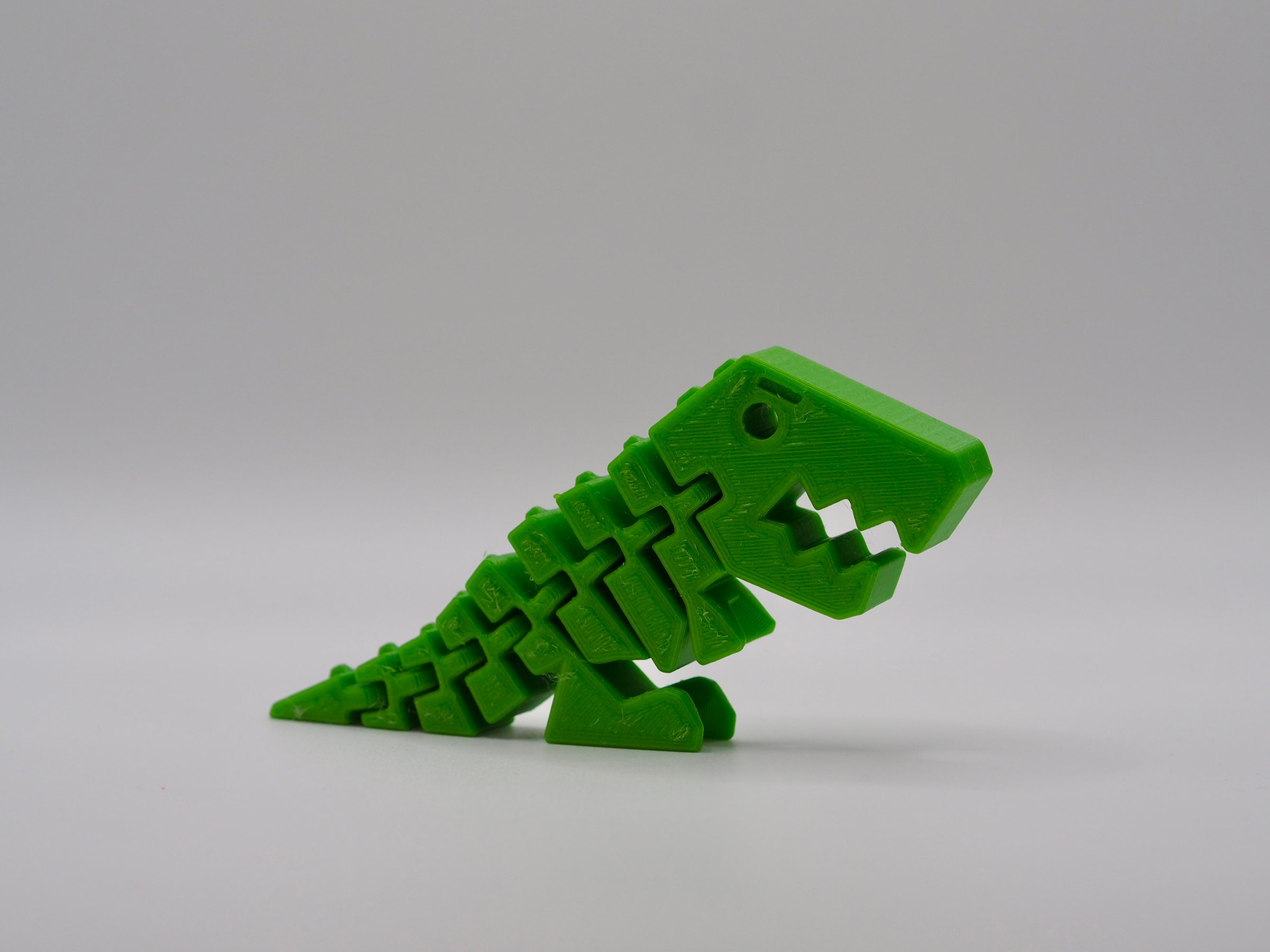 This image captures a vibrant green 3D printed dinosaur toy in a playful and dynamic pose, illustrating creativity and modern technological innovation in printing.