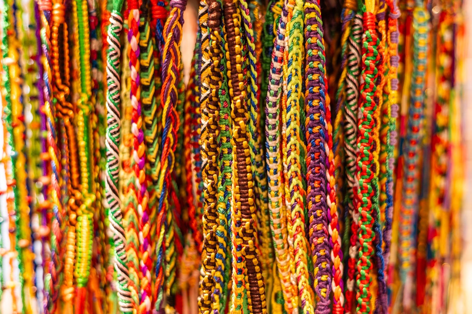 Colorful woven bracelets hang in a display. The intricate patterns feature various bright colors, showcasing craftsmanship and creativity.