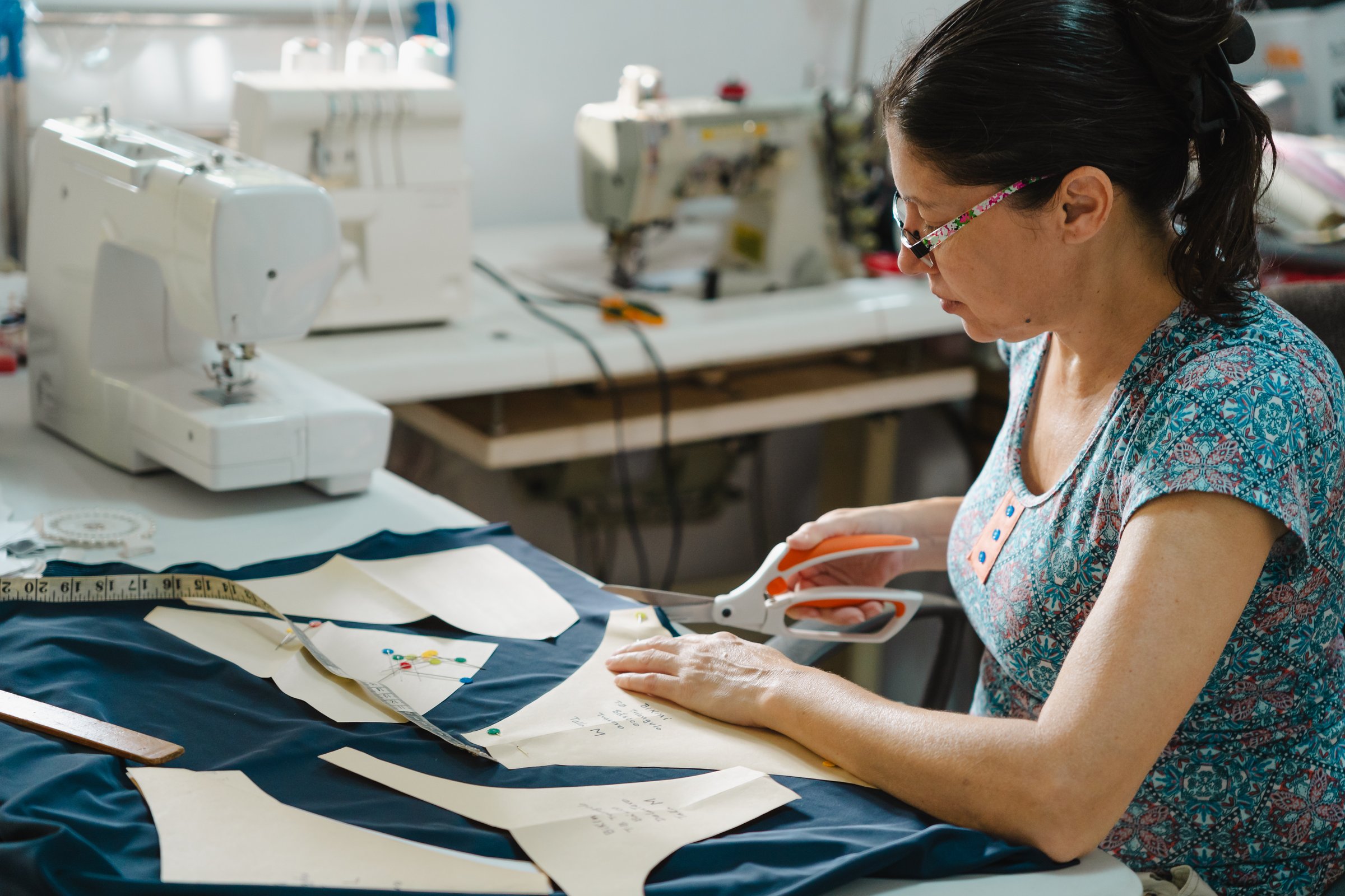 Mid-age latin hispanic woman working in a sewing workshop. Using professional scissors to cut dark fabric. Fashion design and small business concept.