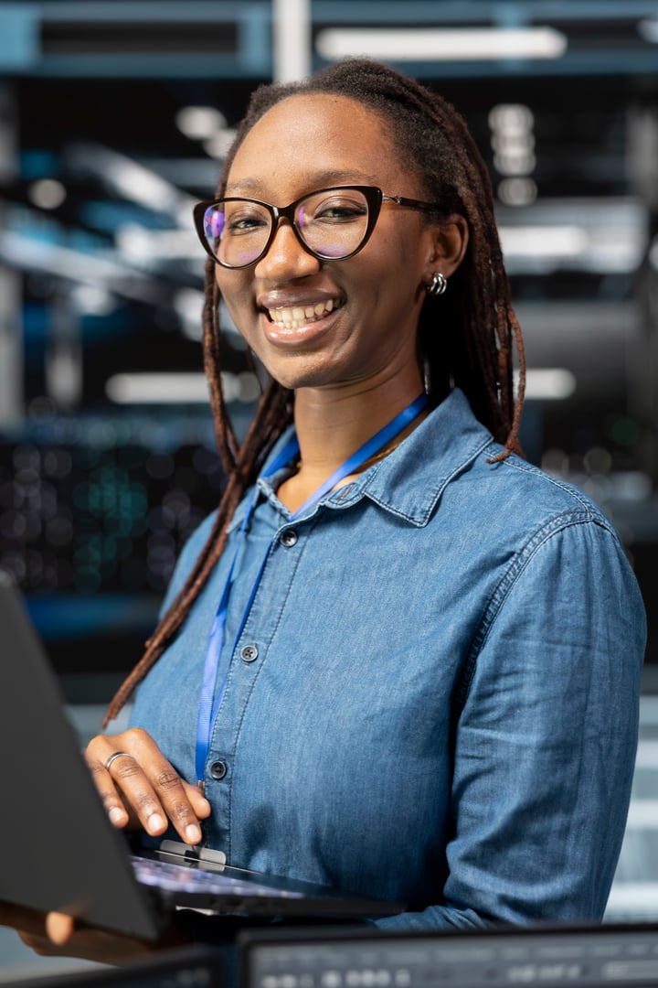 Portrait of smiling technician in data center monitoring system performance with laptop, identifying bottlenecks. Happy server hub employee troubleshooting errors, implementing optimizations