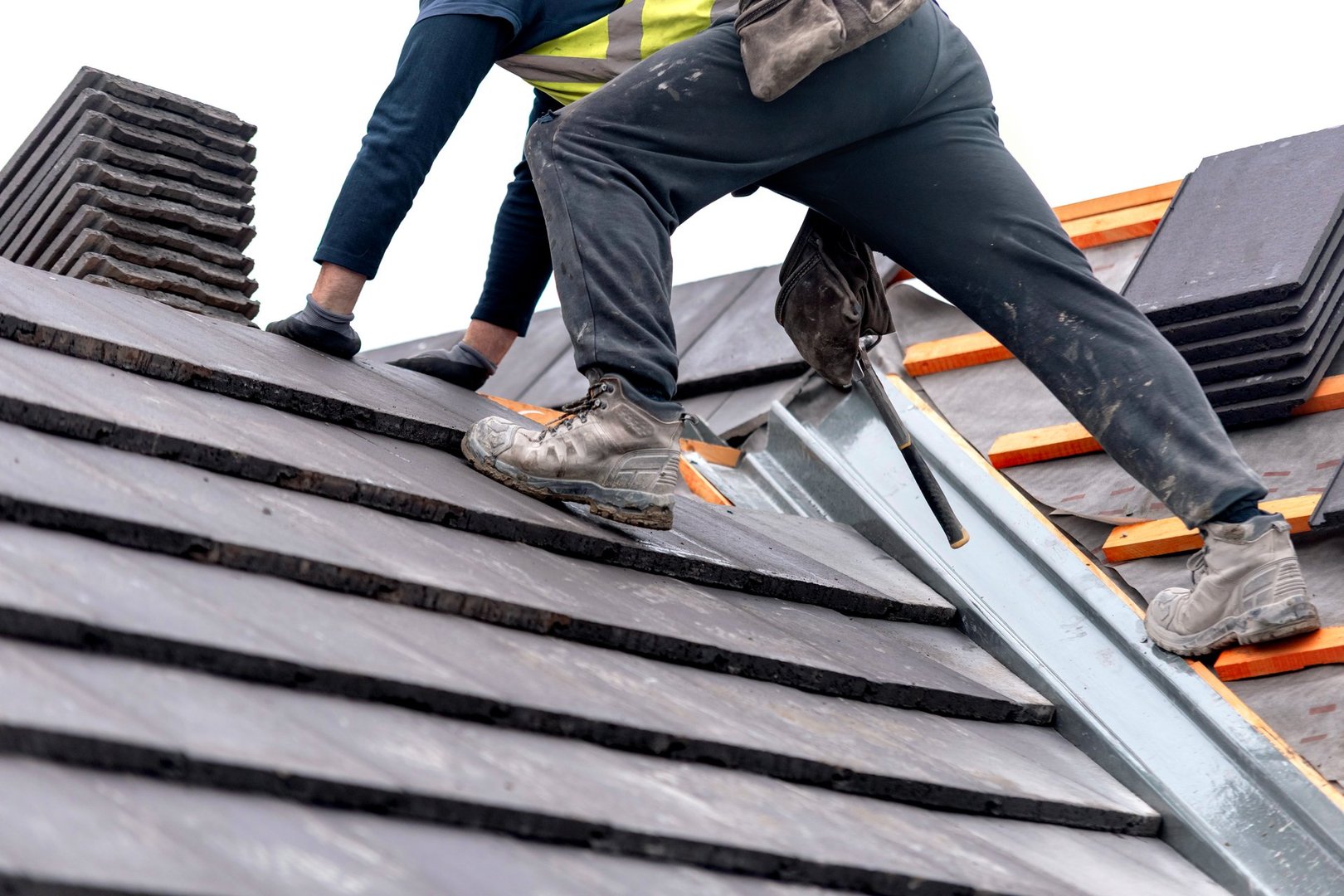 Construction worker carefully places roof tiles on a sloped surface while standing on top of a building showcasing the effort involved in roofing work