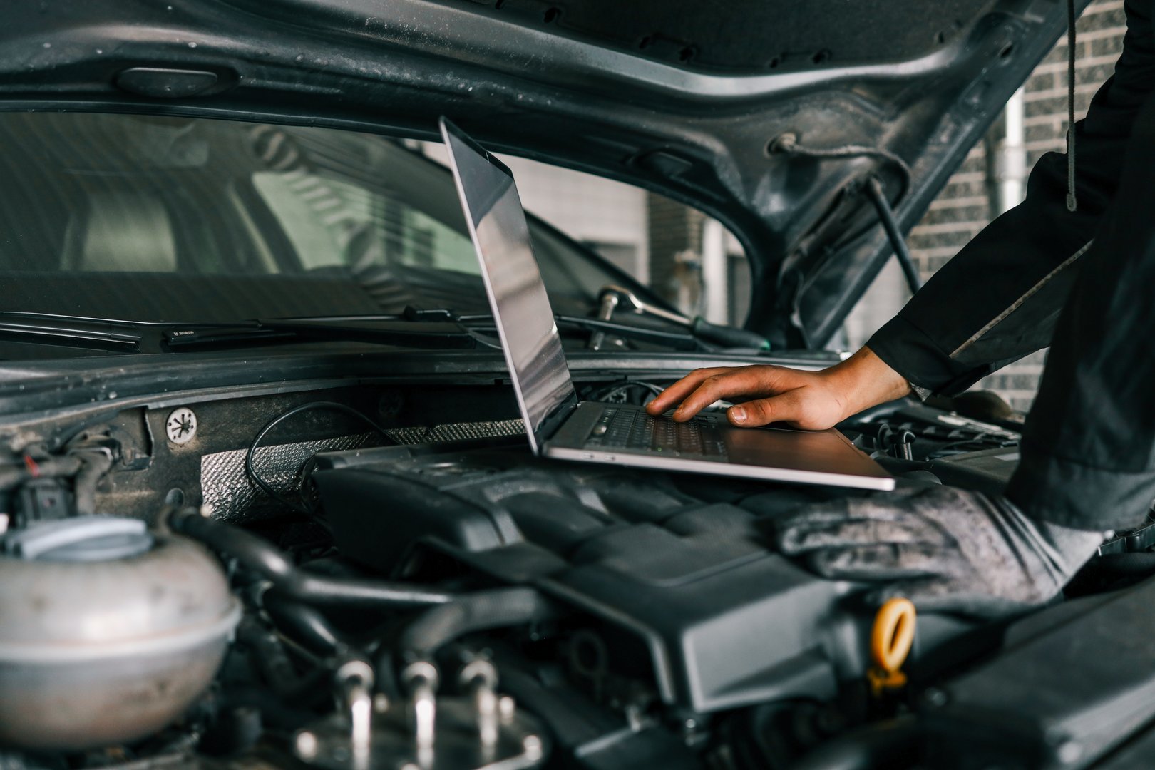 A mechanic using a laptop on a car engine for diagnostics in a garage. Highlights the use of technology in modern vehicle maintenance and repair.