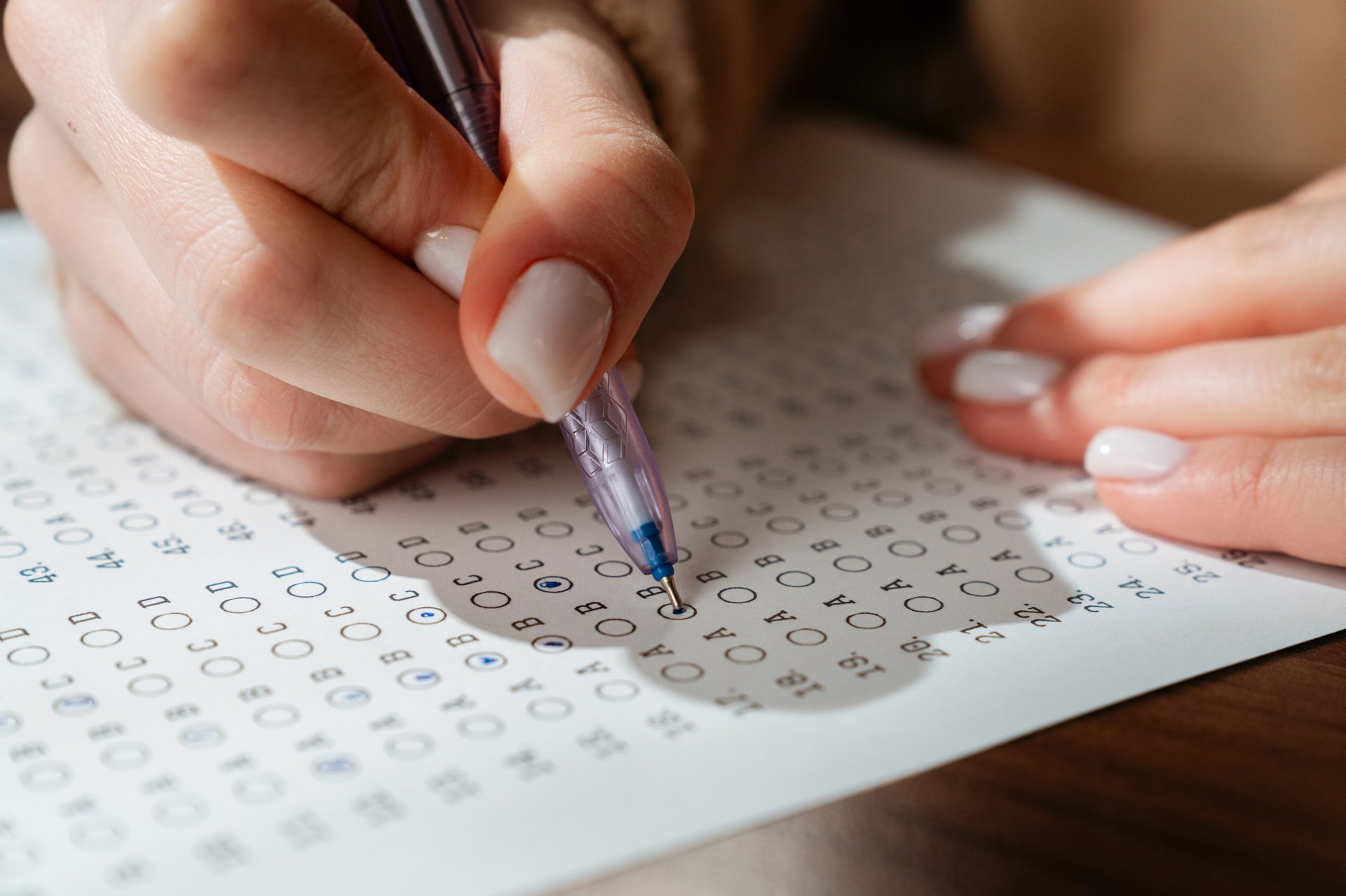 A woman is using a pen to fill out an answer sheet for a standardized test, focusing on precision and accuracy.
