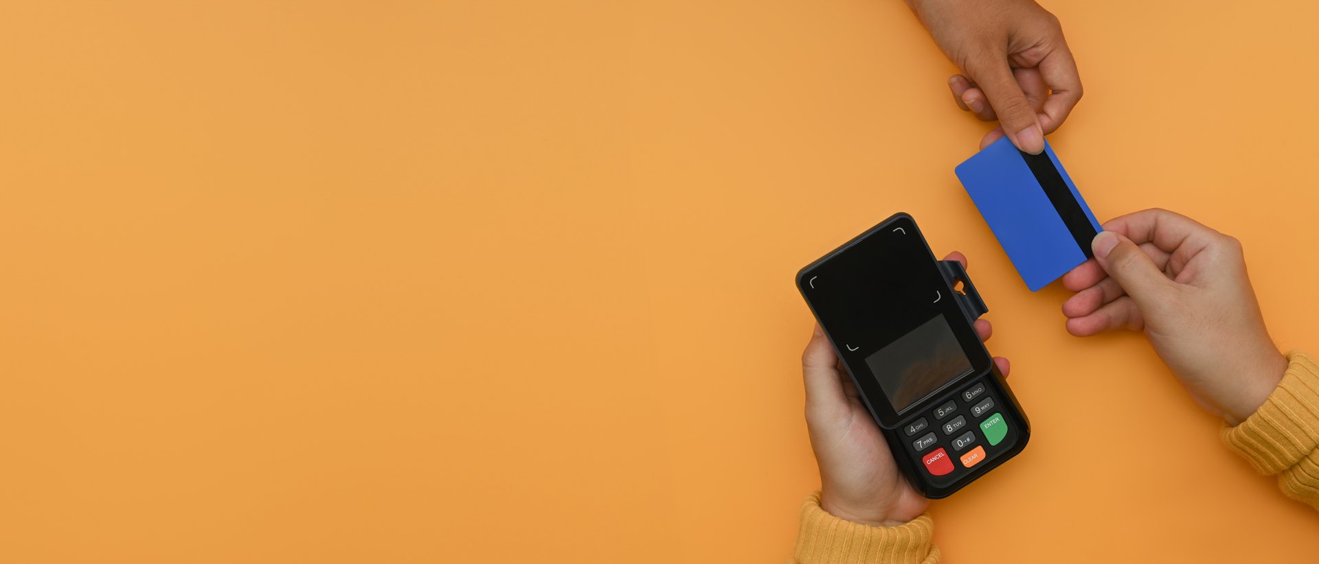 Overhead view of customer paying with with credit card on yellow background.