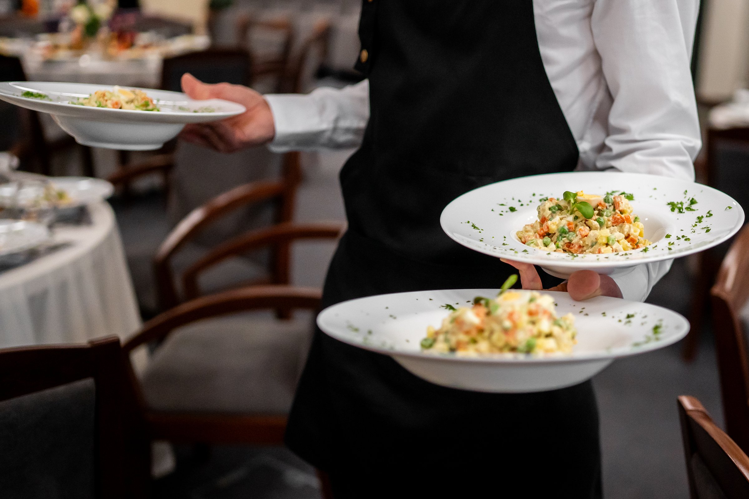 Waiter in white shirt and black apron serving three colorful plated meals in a restaurant. Professional food service, hospitality, and dining atmosphere.