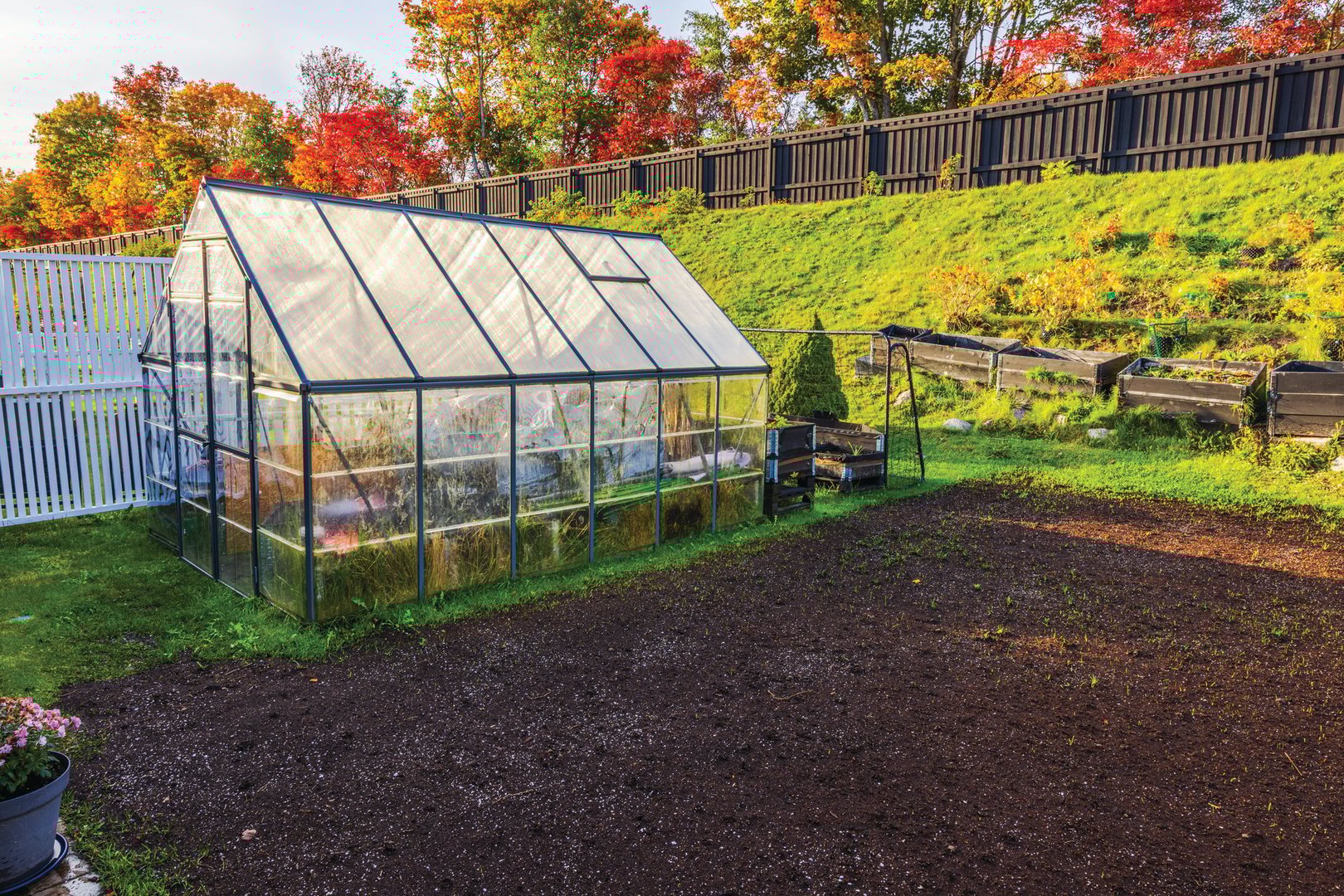 Greenhouse prepared for winter with stored items, set in an autumn garden with colorful trees and empty flowerbeds. Sweden.