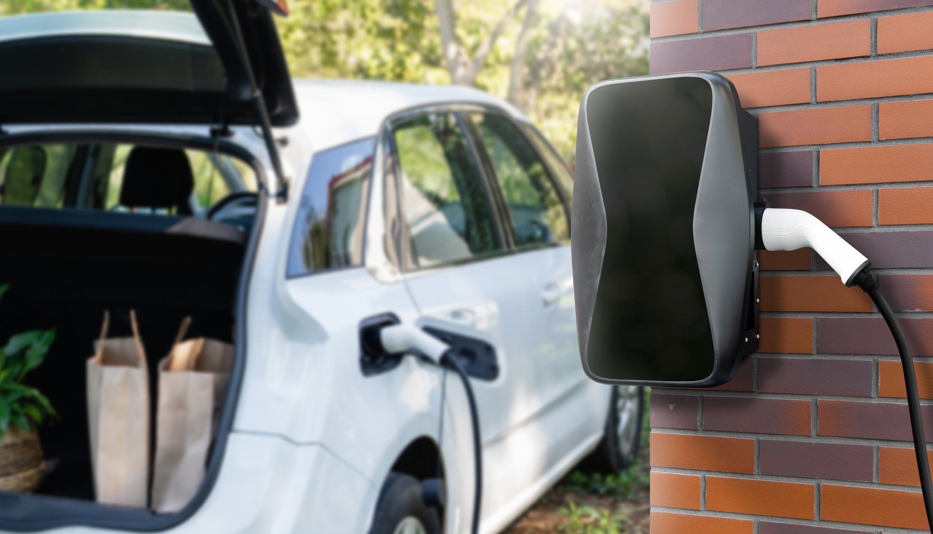 Charging electric car next to house with charging station on the wall.