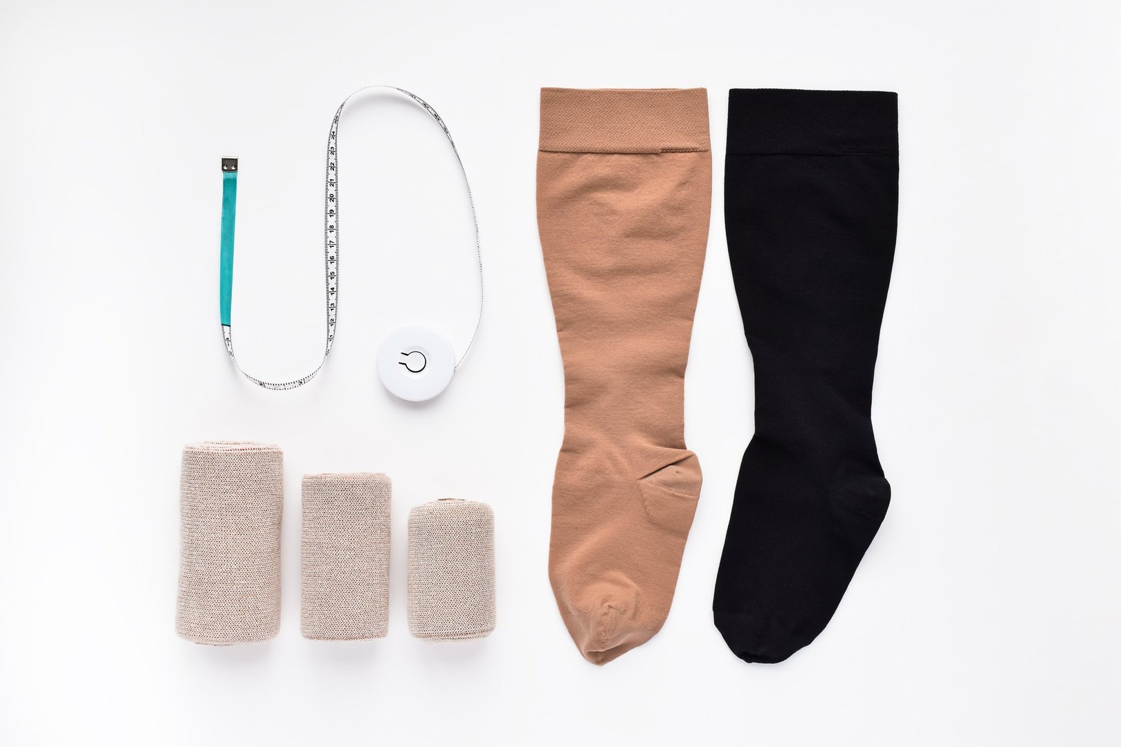 Lymphedema management supplies on white background, knee-high socks, compression wraps and tape measure
