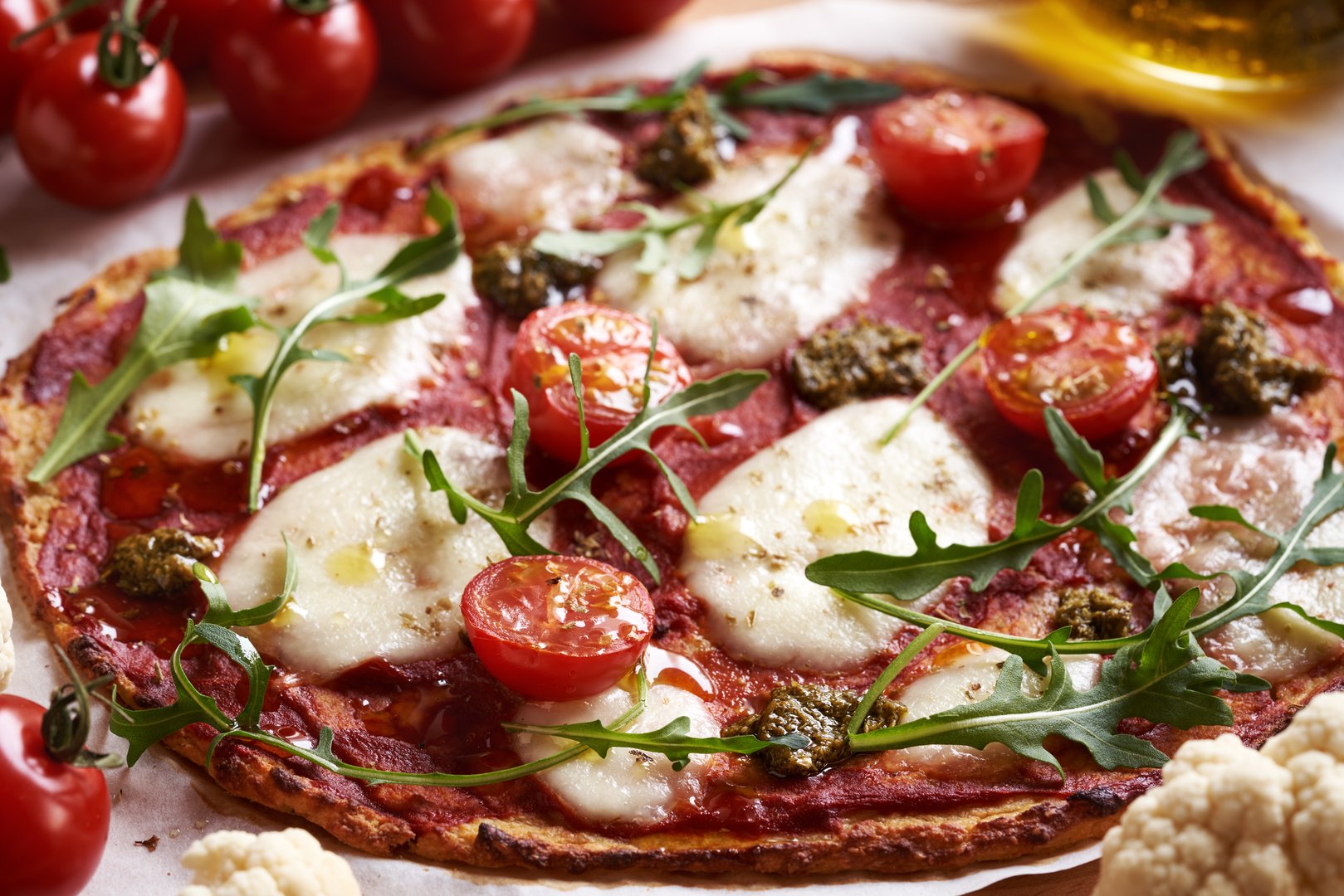 Homemade gluten-free pizza made of cauliflower, celery root, cheese and almond meal, topped with mozzarella, tomatoes and arugula