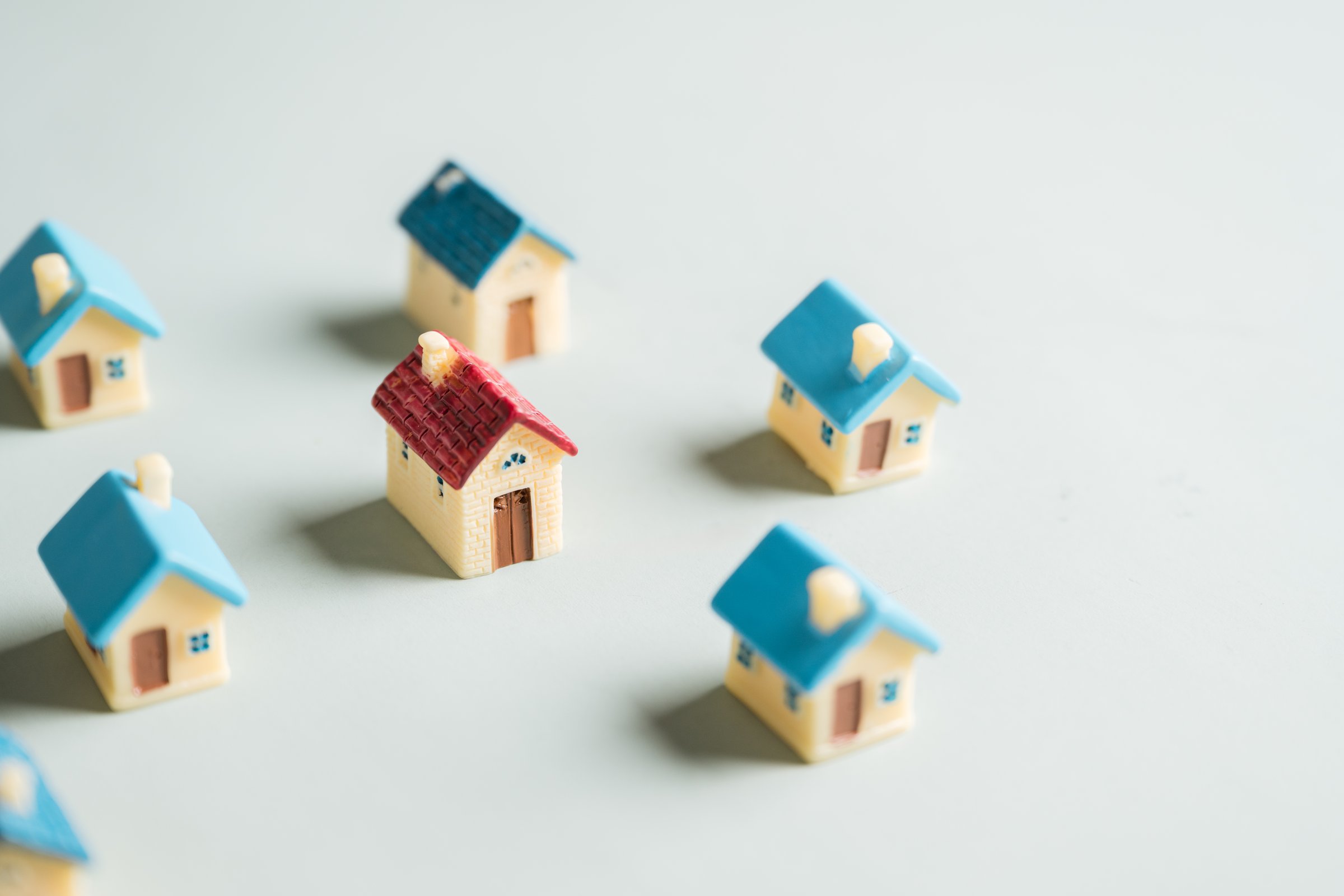 Property management. Real estate investment. Estate planning. Property planning. A row of small houses are lined up on a gray surface. One house is missing. The houses are all different colors.