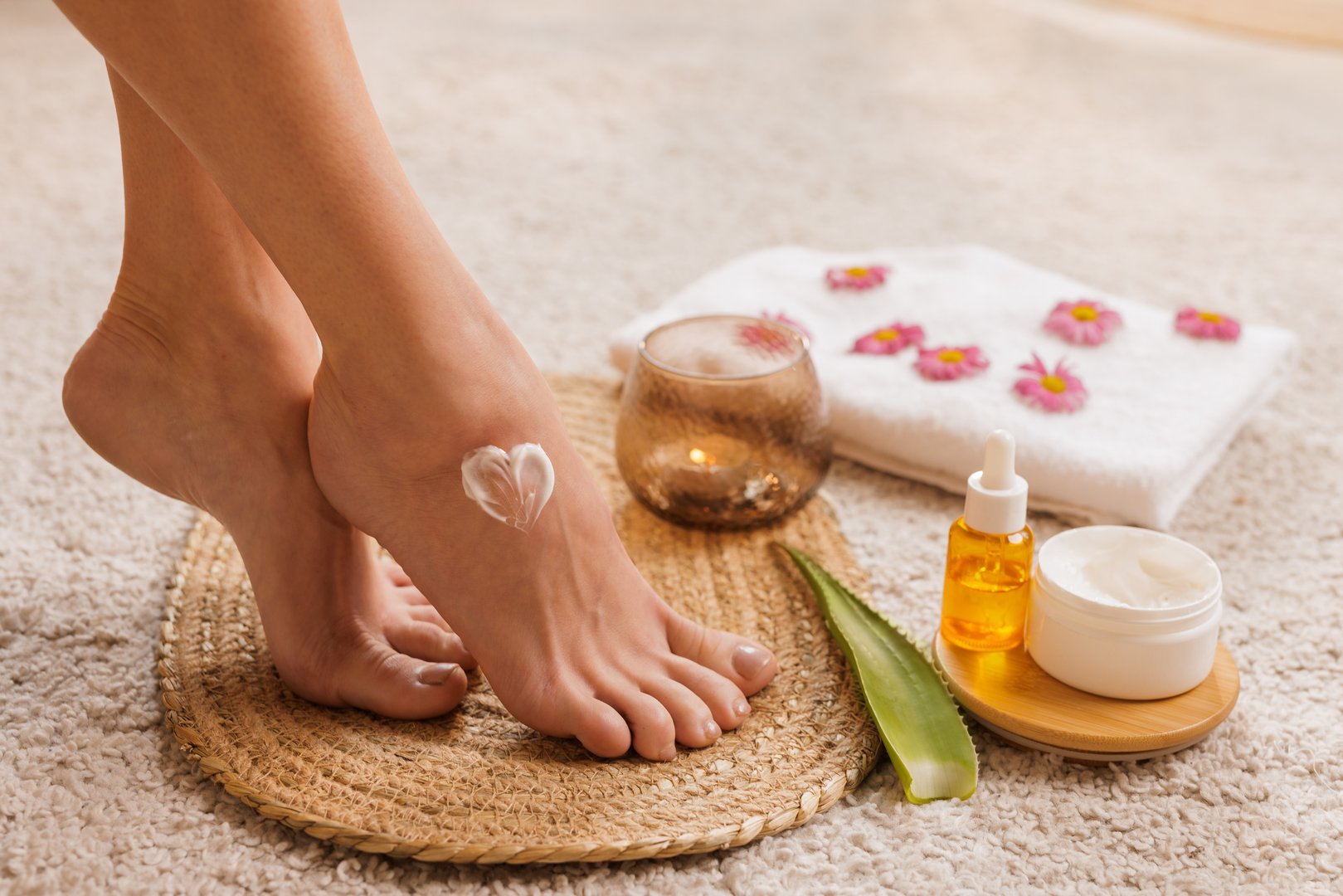 Heart-shaped foot cream, aloe, oil, towel, and candle in cozy home spa setting. Natural self-care and skin hydration concept.