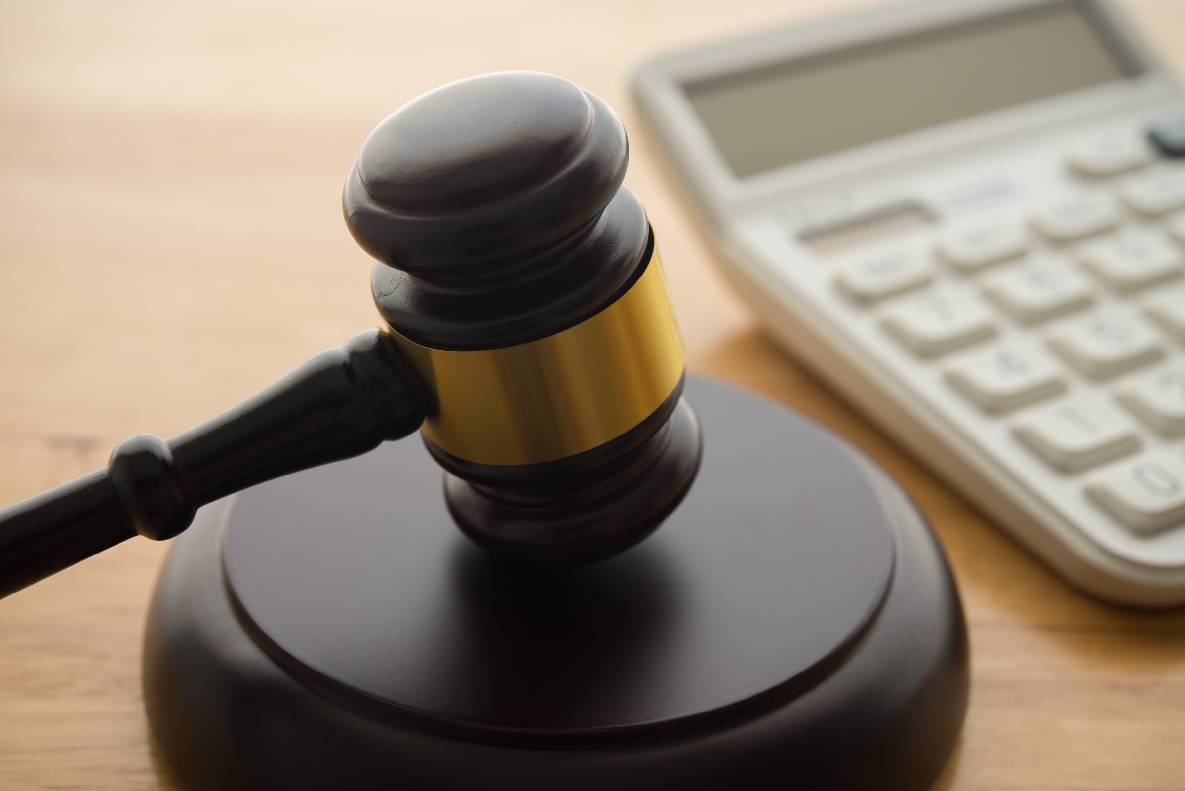 Gavel hammer judge and white calculator on wooden table background. Tax law, financial law or regulation, creative accounting, corruption, bribe, bankruptcy, penalty and so on concept.