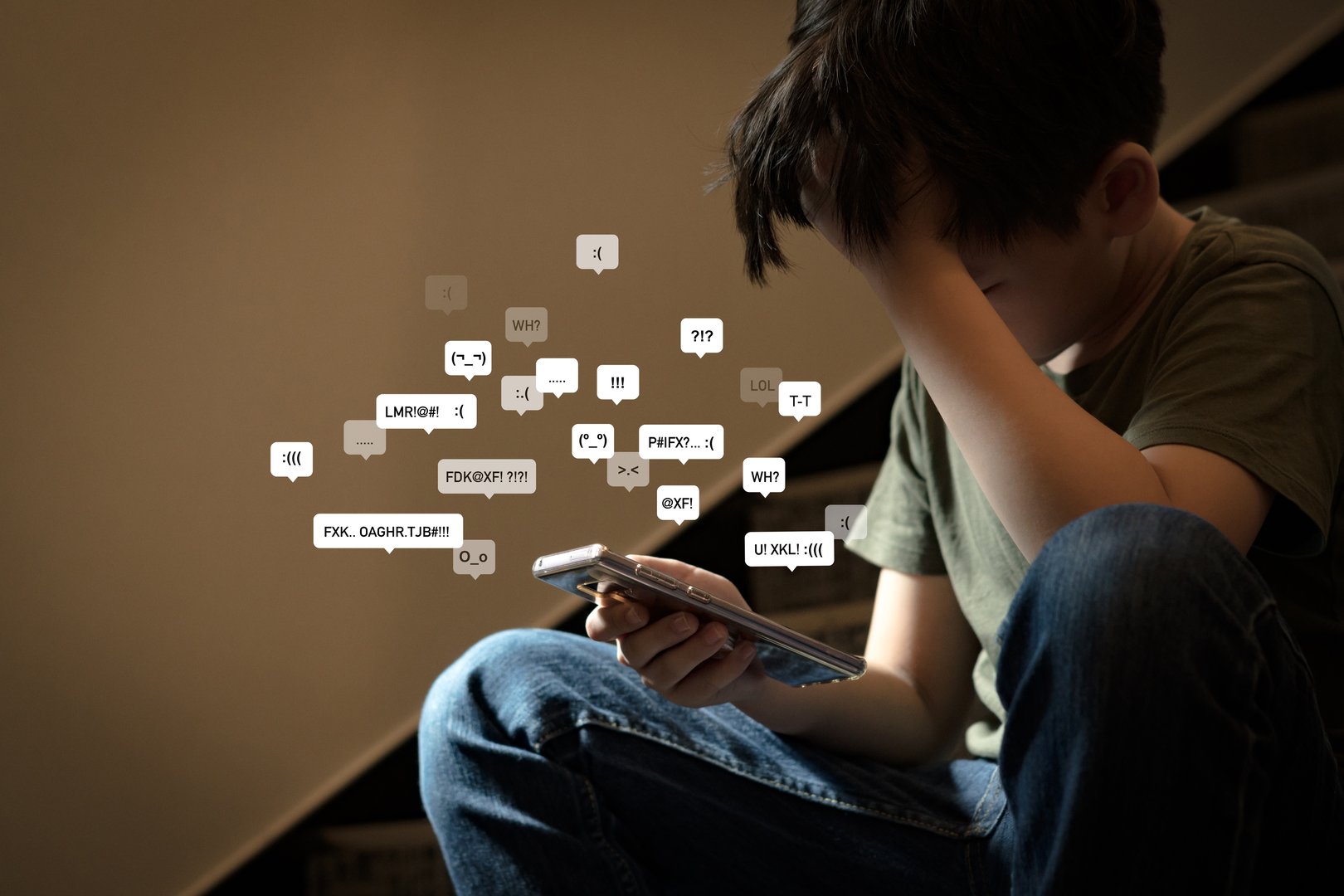 Asian teenage boy sitting at stair, covering his face with hands, face down, holding smartphone in low light feeling frustrated, lonely, stress and depressed. Cyber bullying concept.