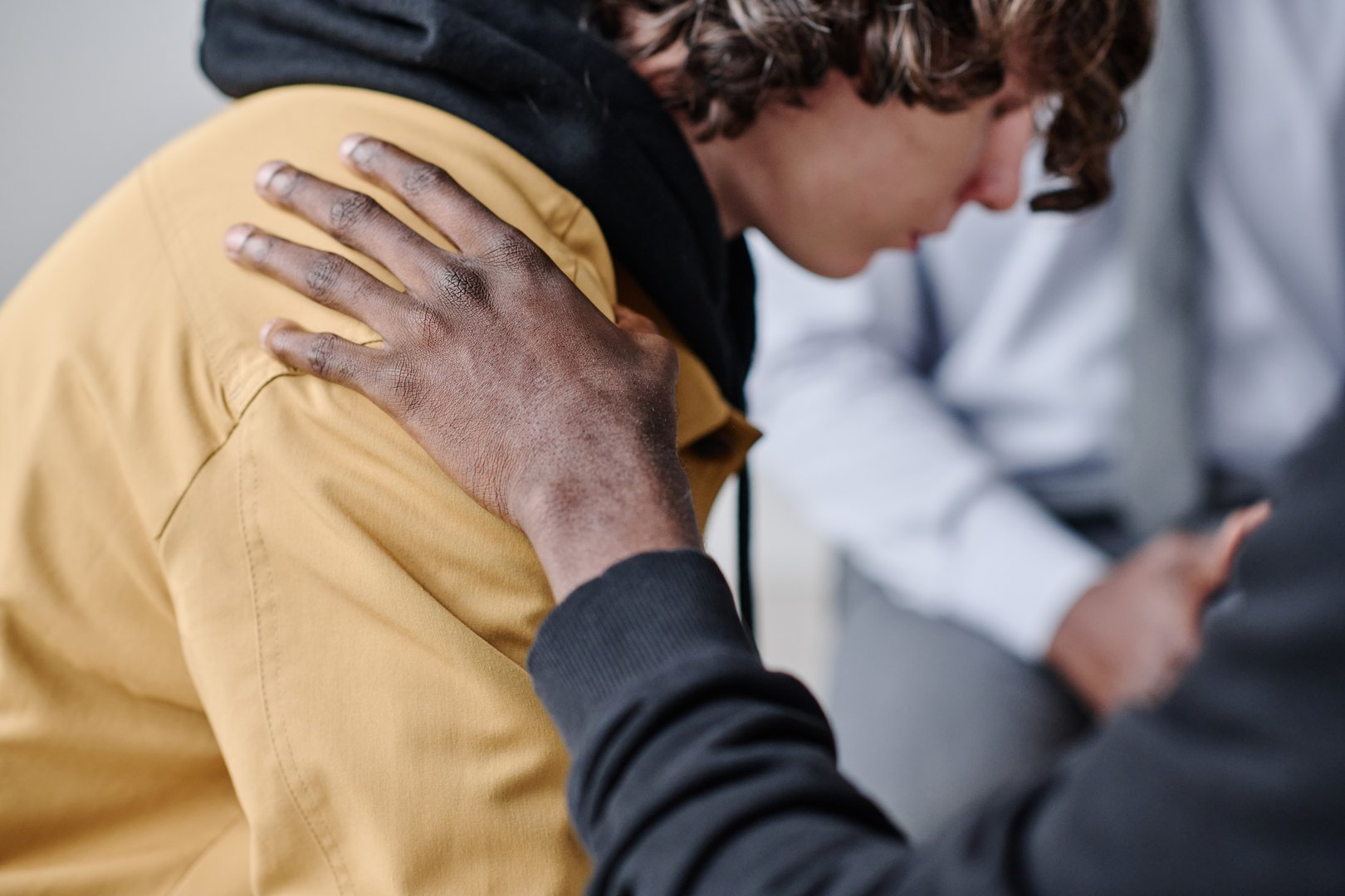 Depressed teenage guy getting support from other people while having visit to psychologist at class