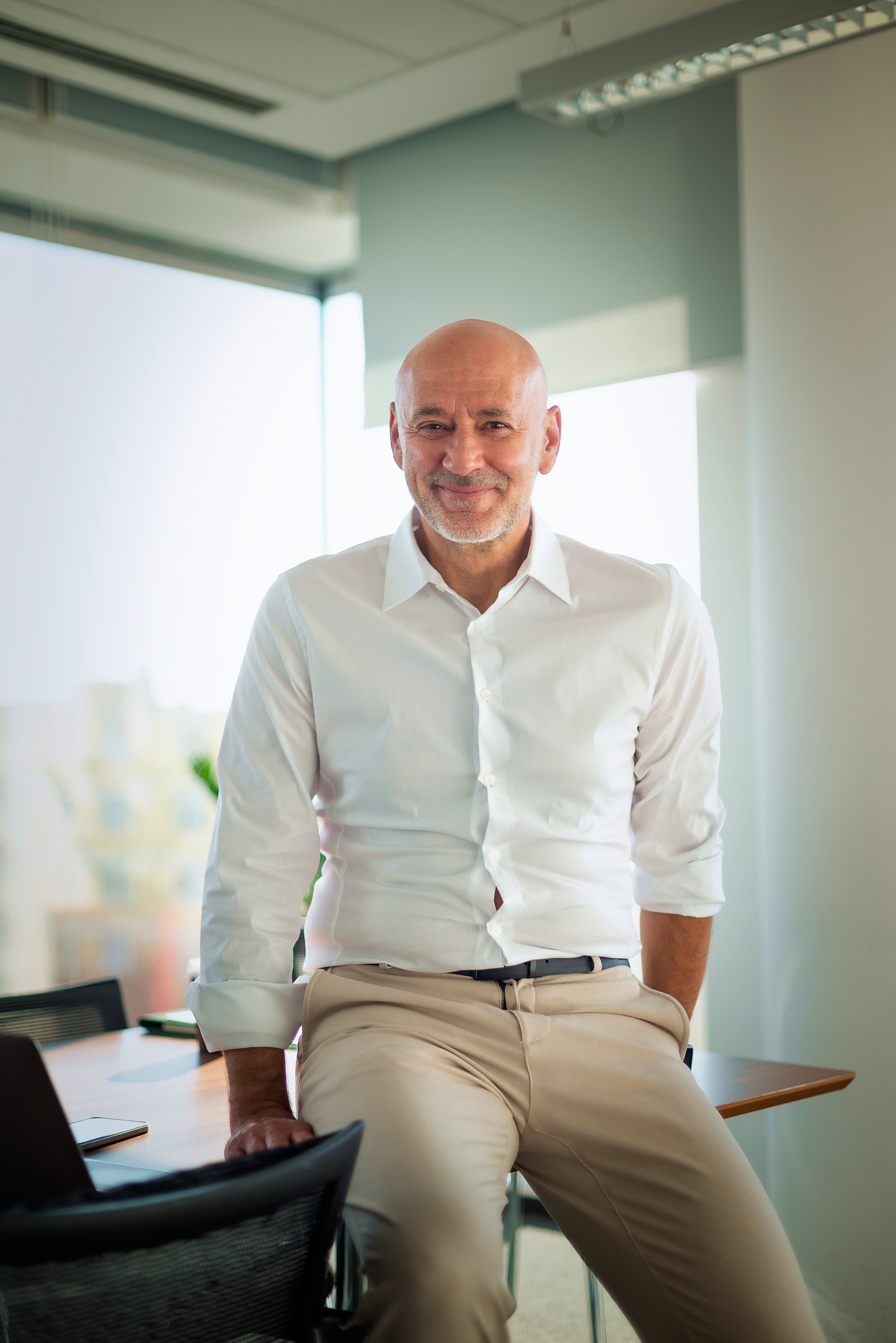 Executive businessman standing at office desk in a modern office. Mid aged professional man wearing shirt and smiling at the camera.