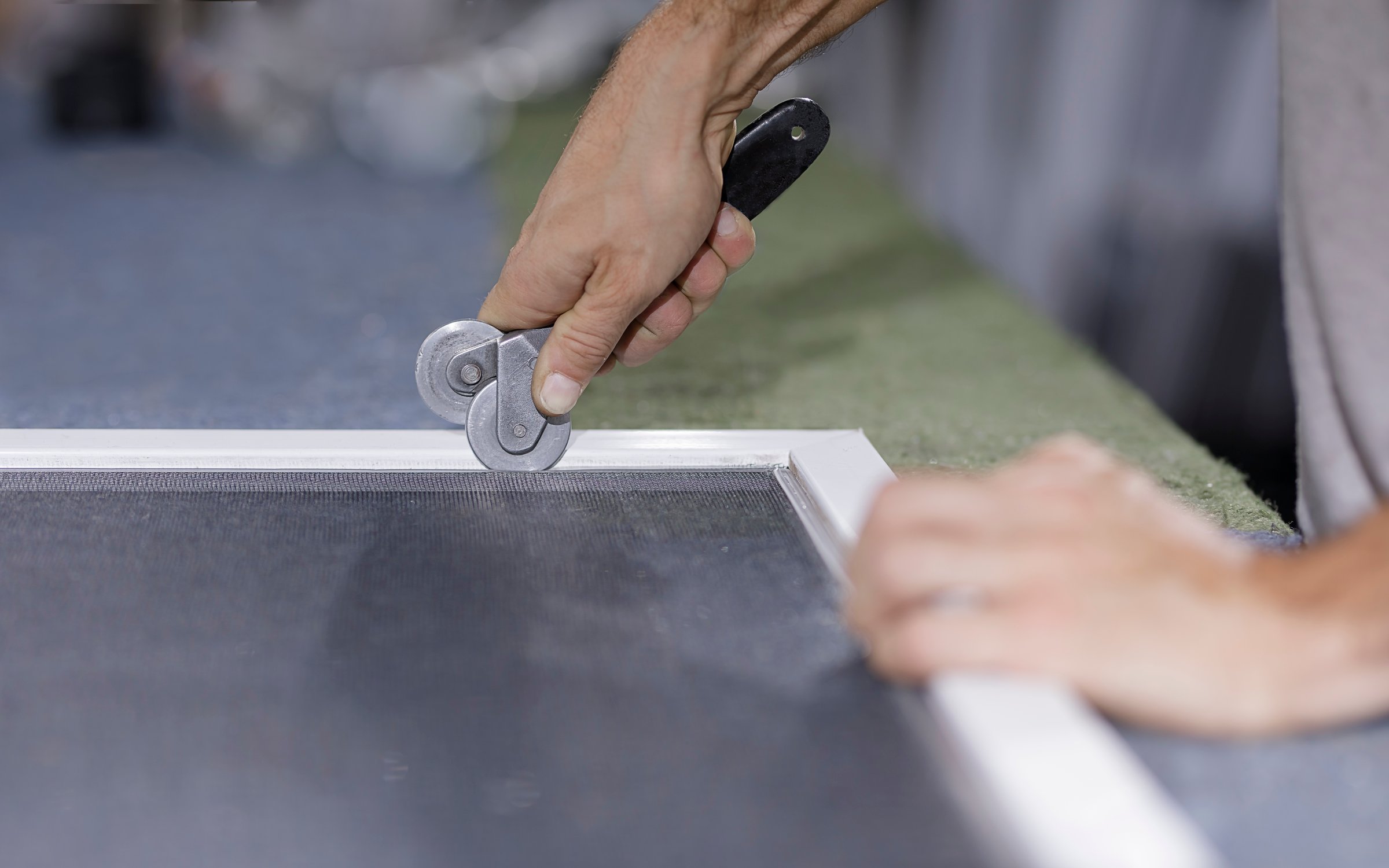 A Man putting together a window screen. You can see a man's hand with a wheel tool to install a mosquito net.