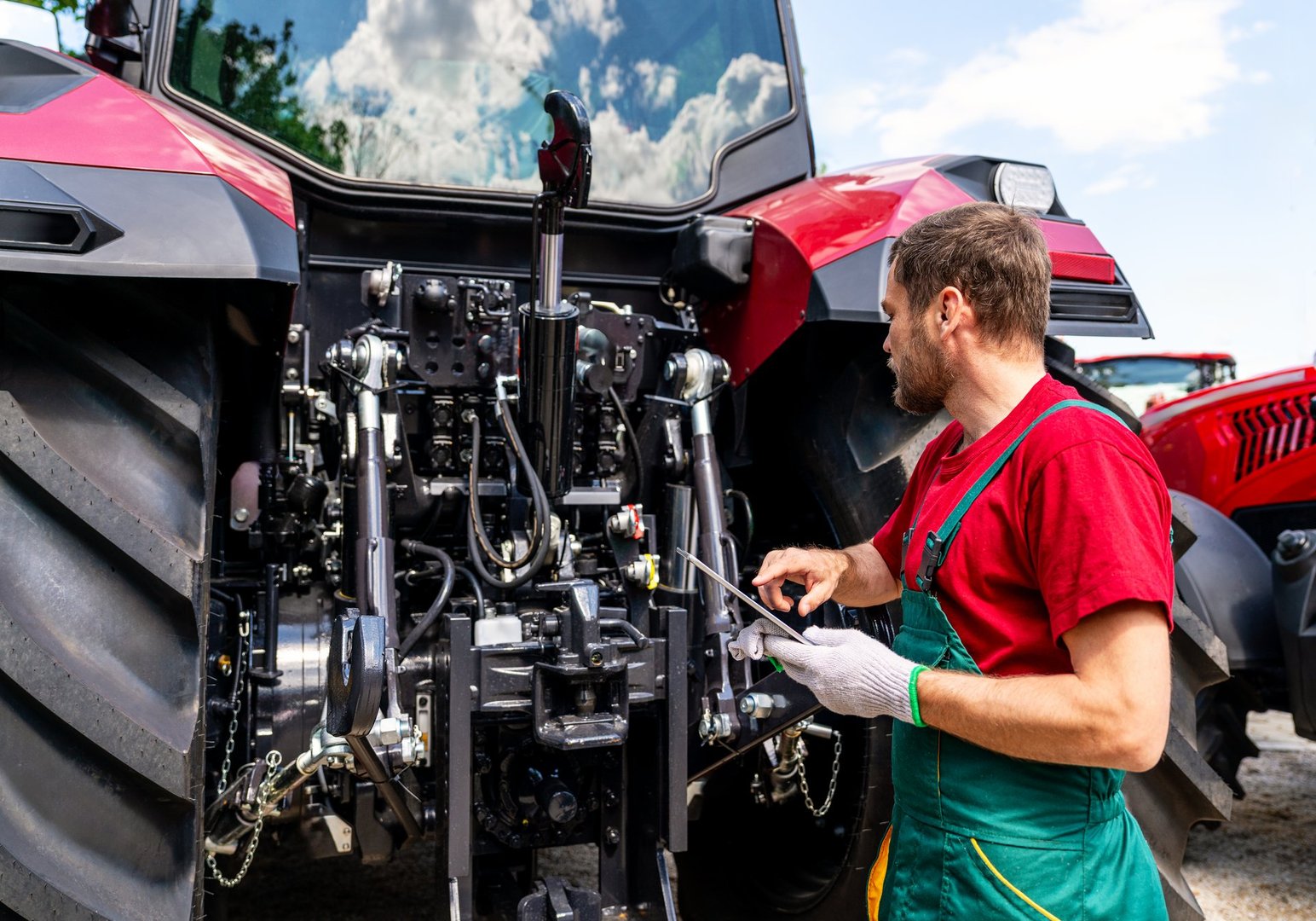 Male mechanic checking farm tractor using digital tablet in rural area