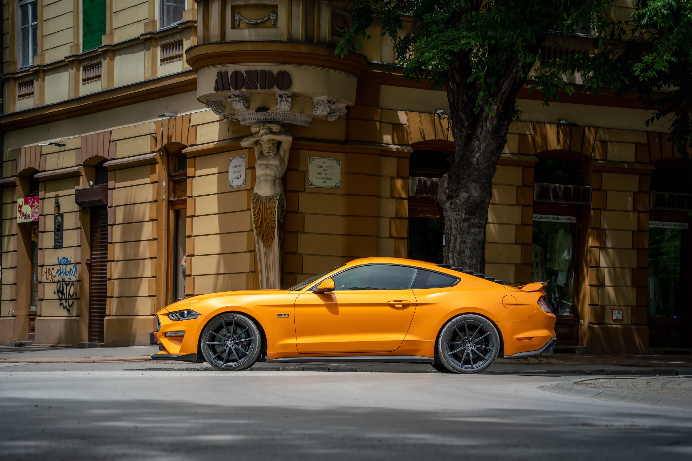 Side view of Ford Mustang GT sixth generation (S550; 2015) in bright orange color is driving down the street of Subotica town, Serbia, 09.06.2024