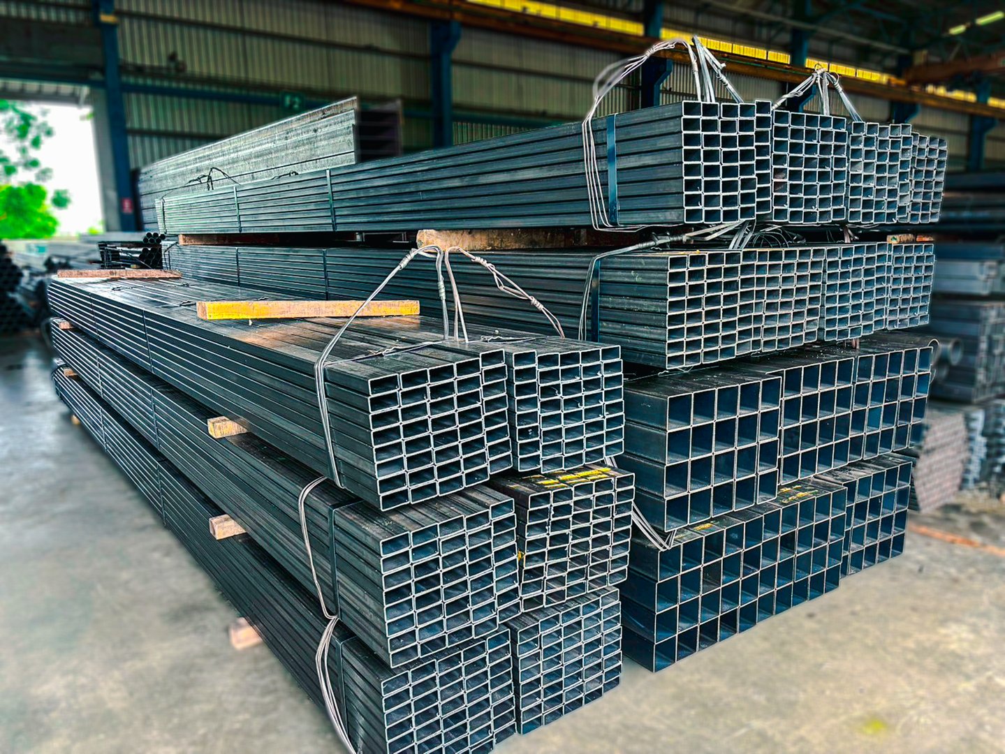 Square steel pipes stacked in a warehouse, used in construction and industrial applications. Durable structural metal tubing for building frameworks, furniture, and fabrication projects.