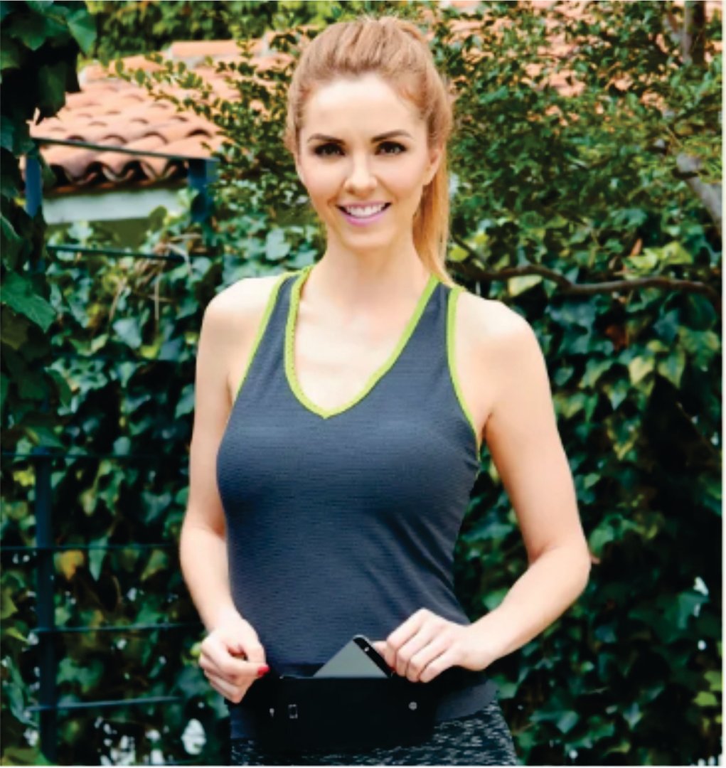 Woman in a sleeveless workout top outdoors, smiling and holding a small black bag with a phone.